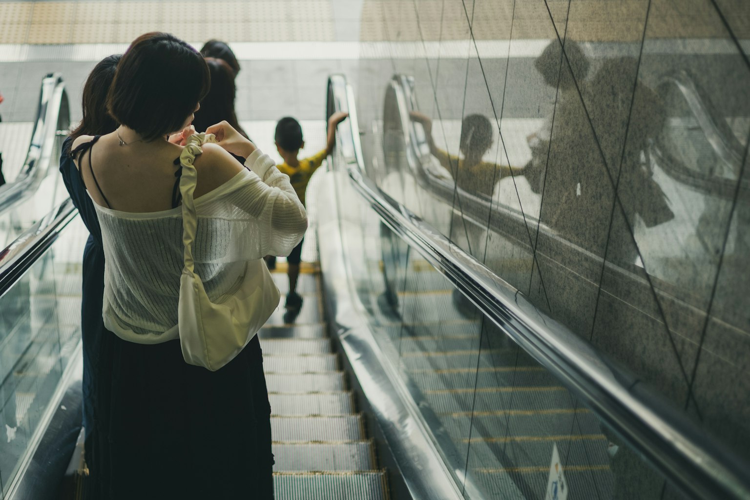 Wanita menuruni eskalator dengan refleksi di kaca