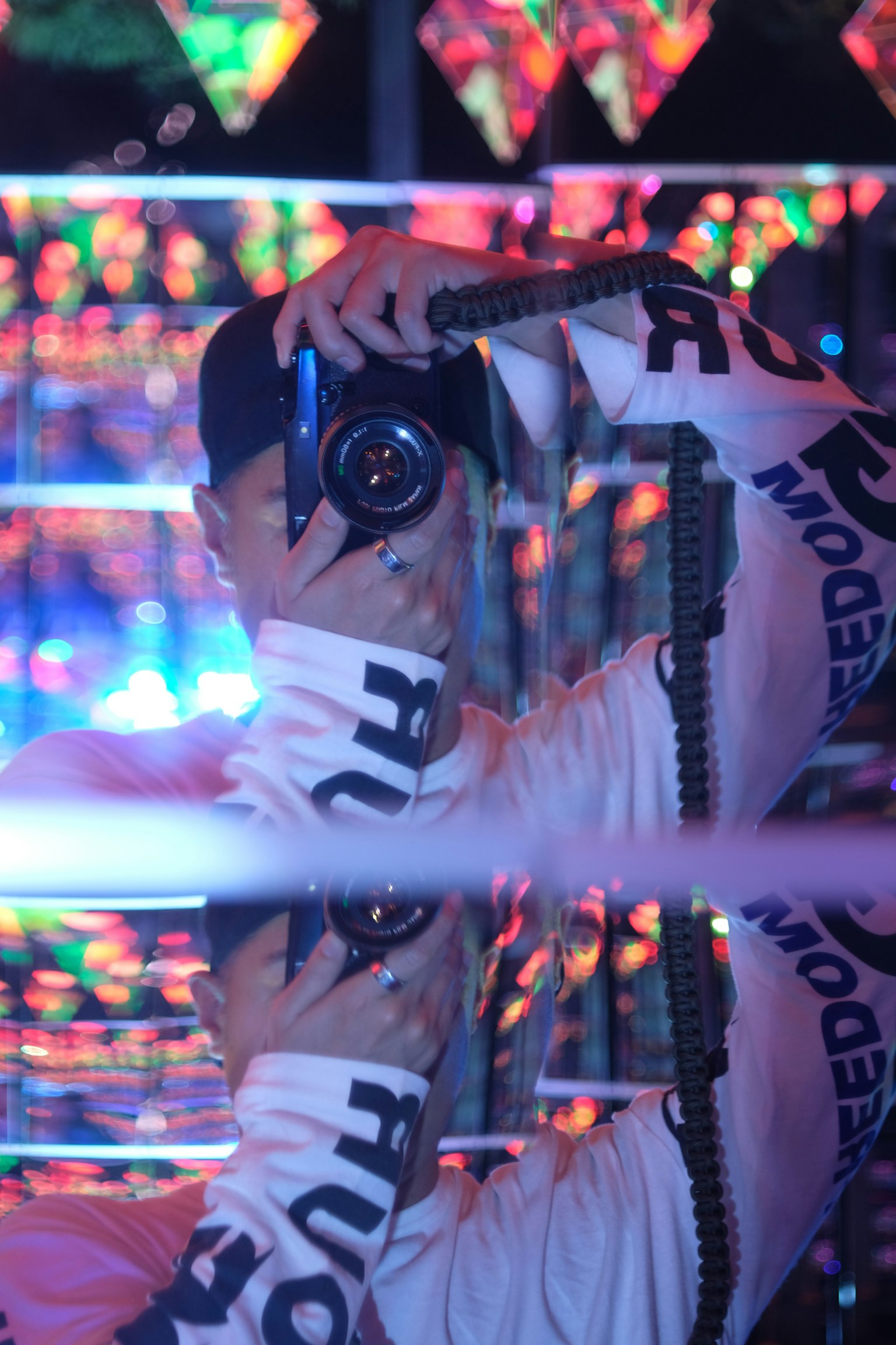 カメラを持った人物が鏡の前で自撮りをしている色とりどりの光の中で