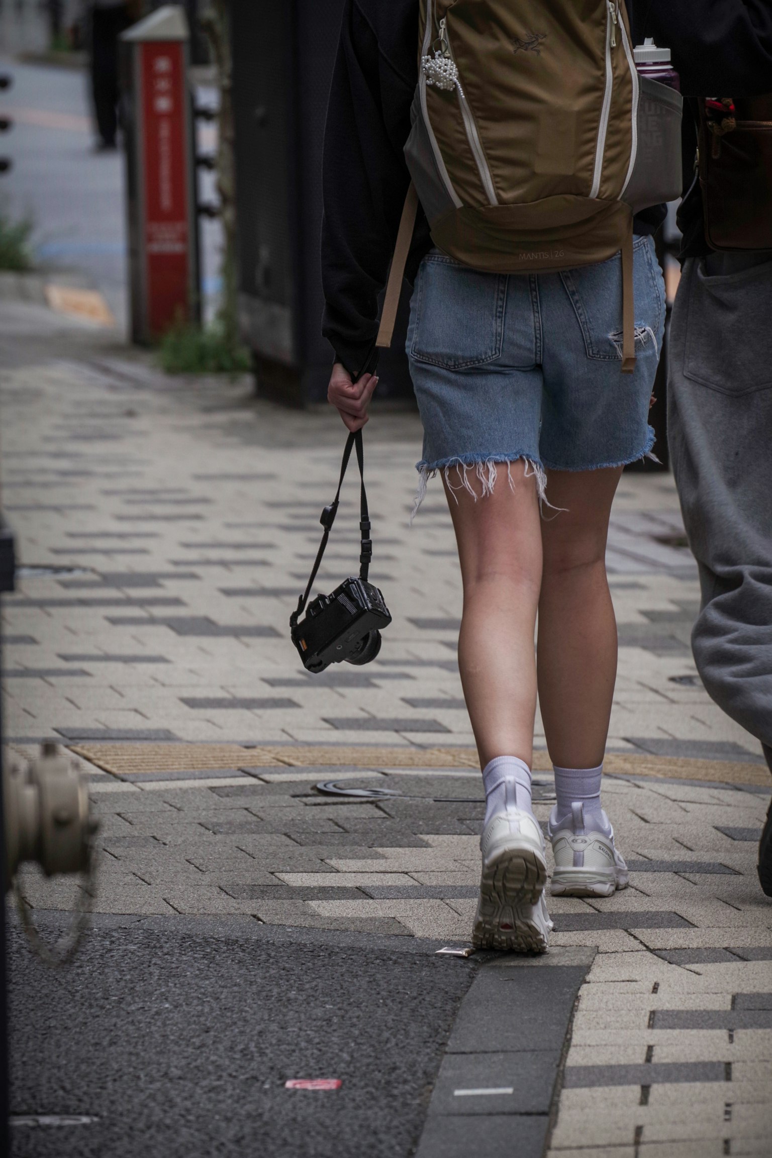 Una persona con pantalones cortos de mezclilla caminando con una cámara en un entorno urbano