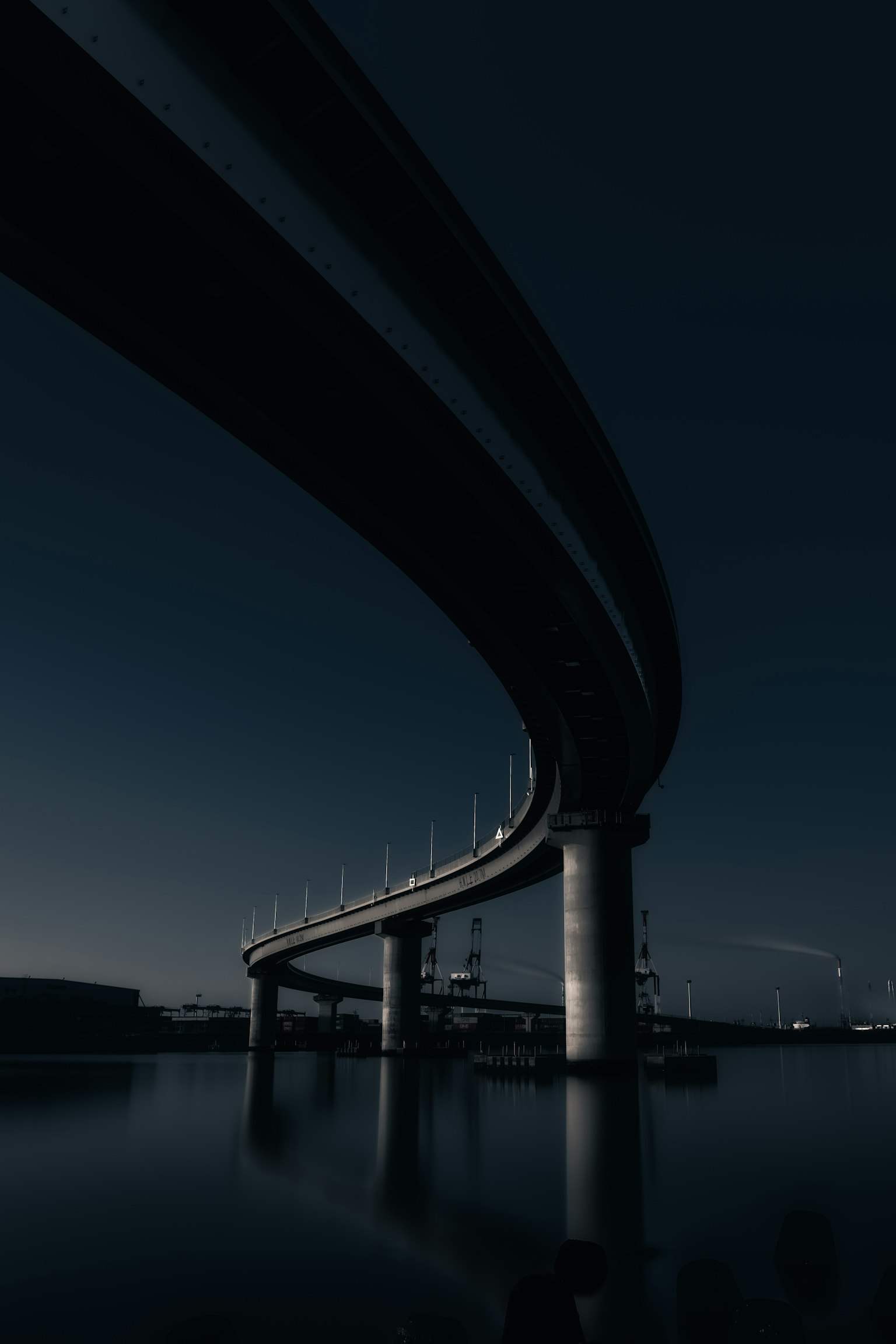 Curved bridge against a dark background with reflections on the water