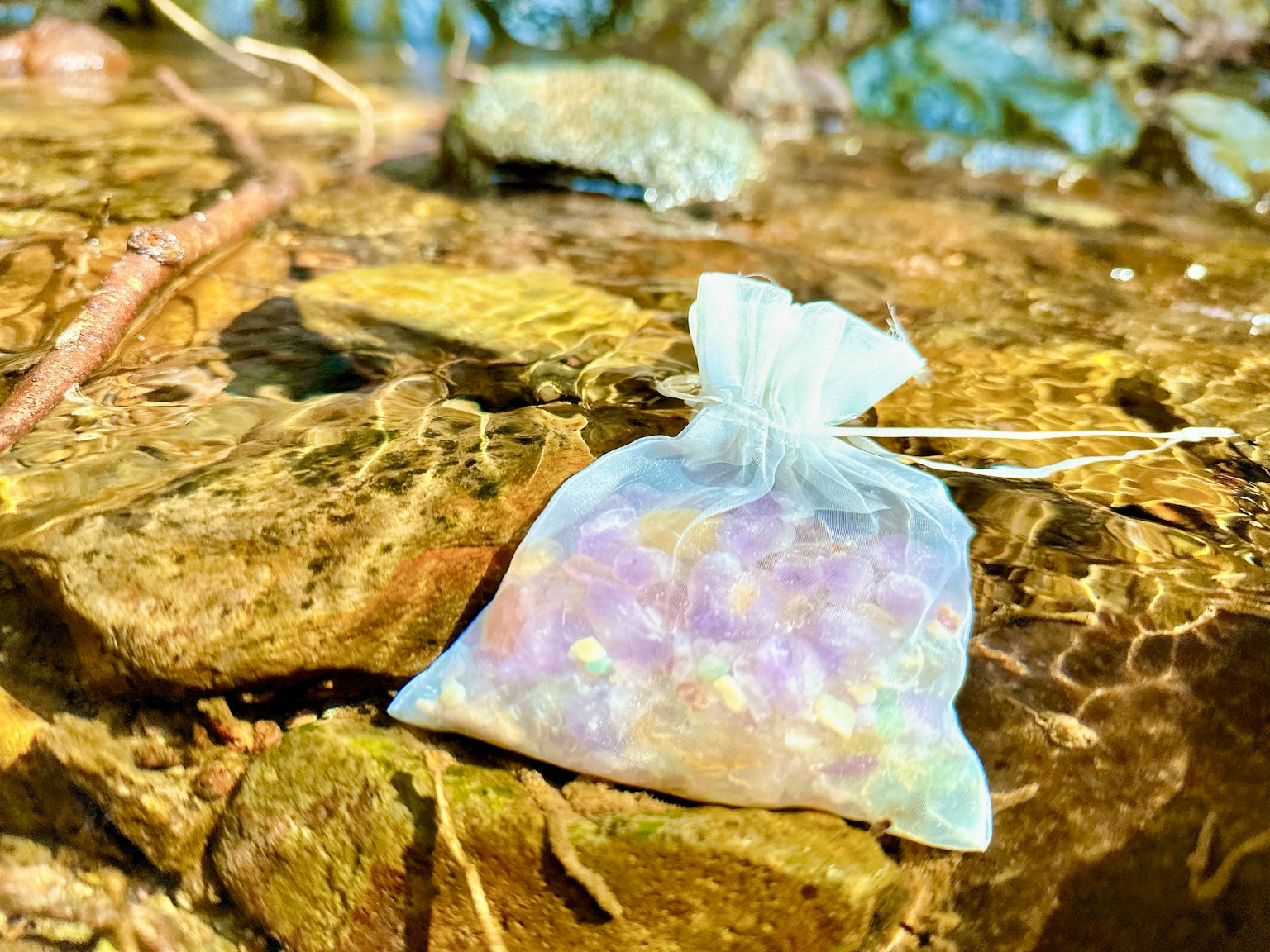 Un sac colorato pieno di gemme appoggiato su una roccia vicino all'acqua