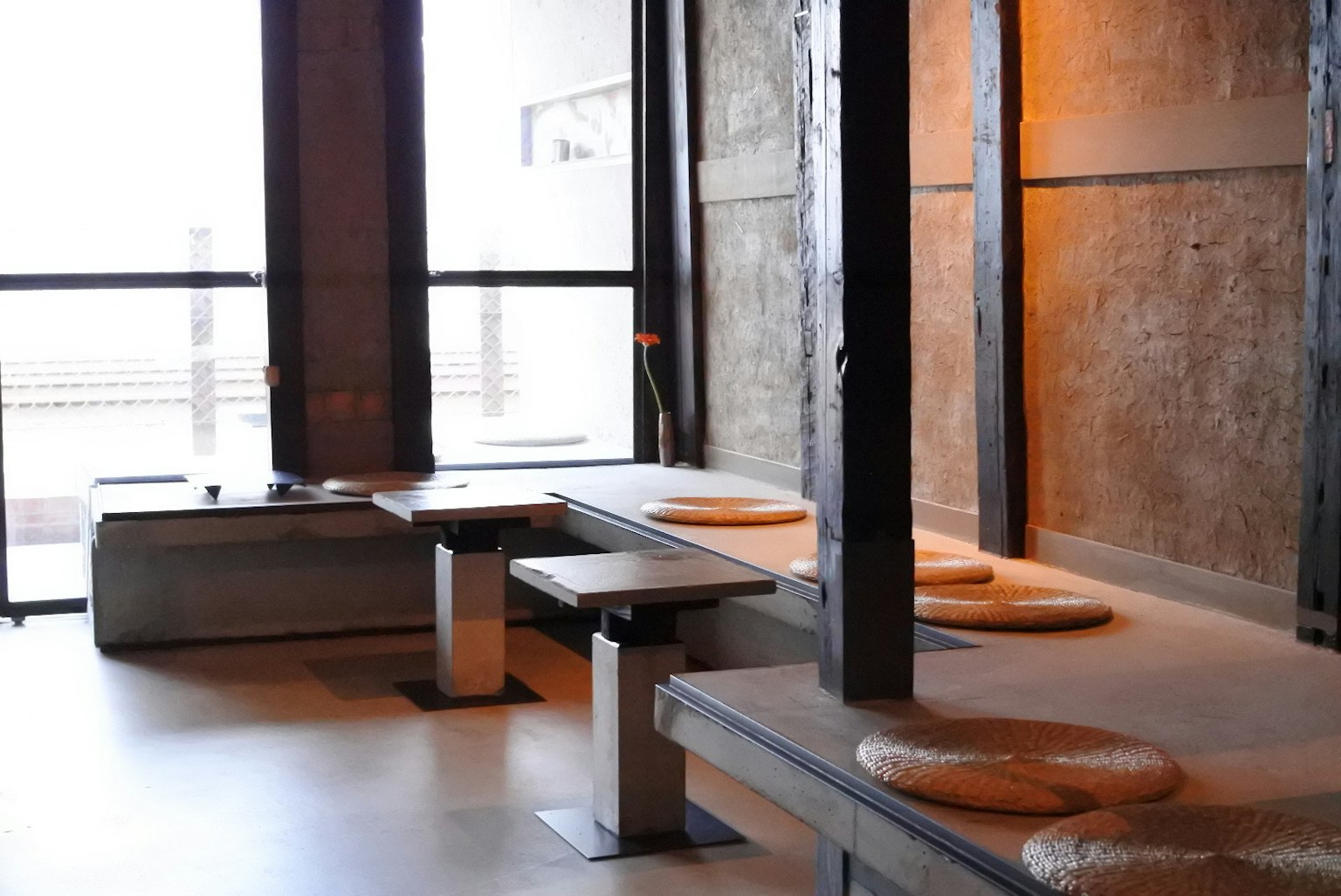 Área de asientos minimalista de café con elementos de madera y concreto luz natural que entra por grandes ventanas