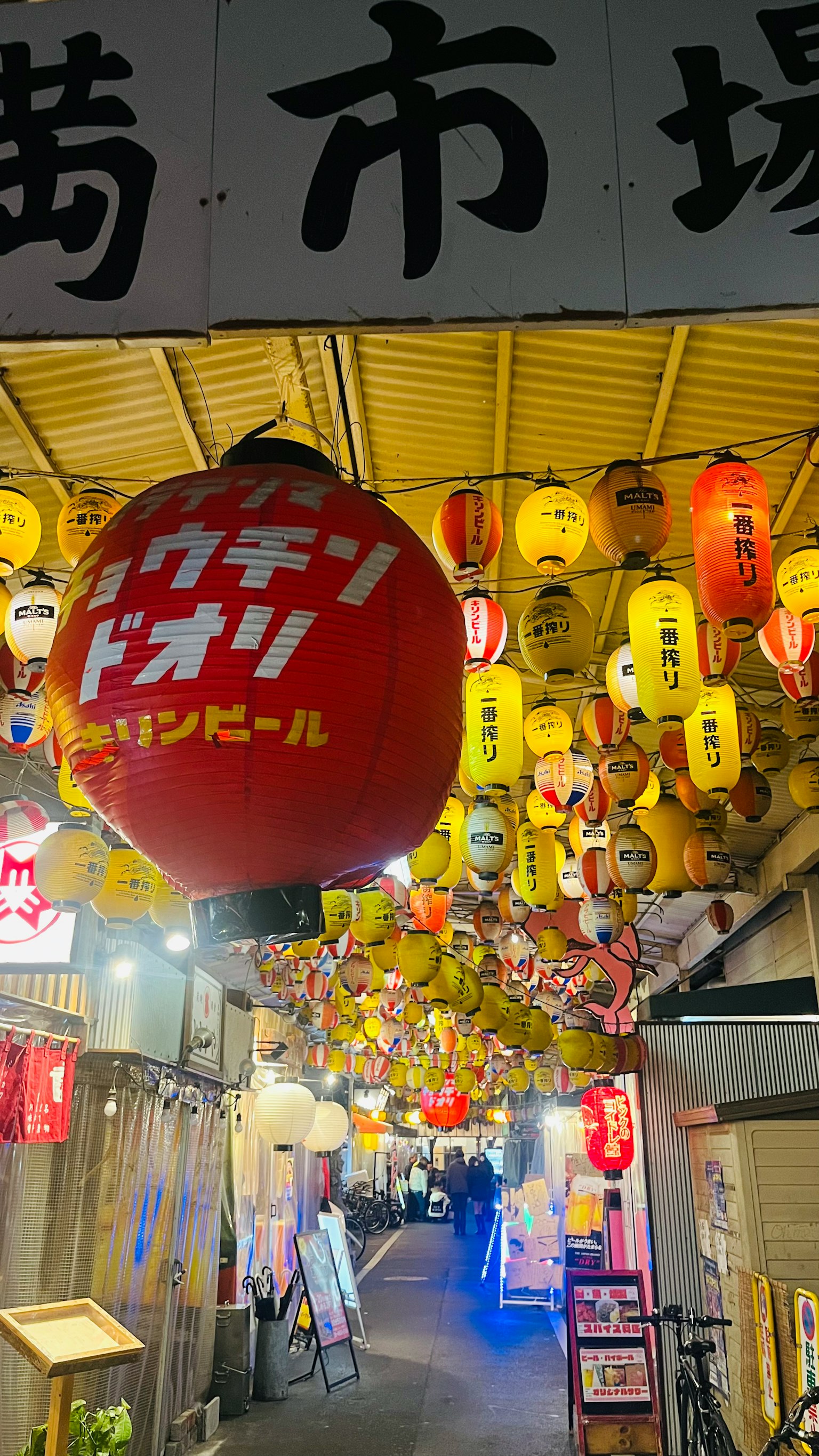 Lanternes colorées suspendues dans une rue bordée de stands de marché