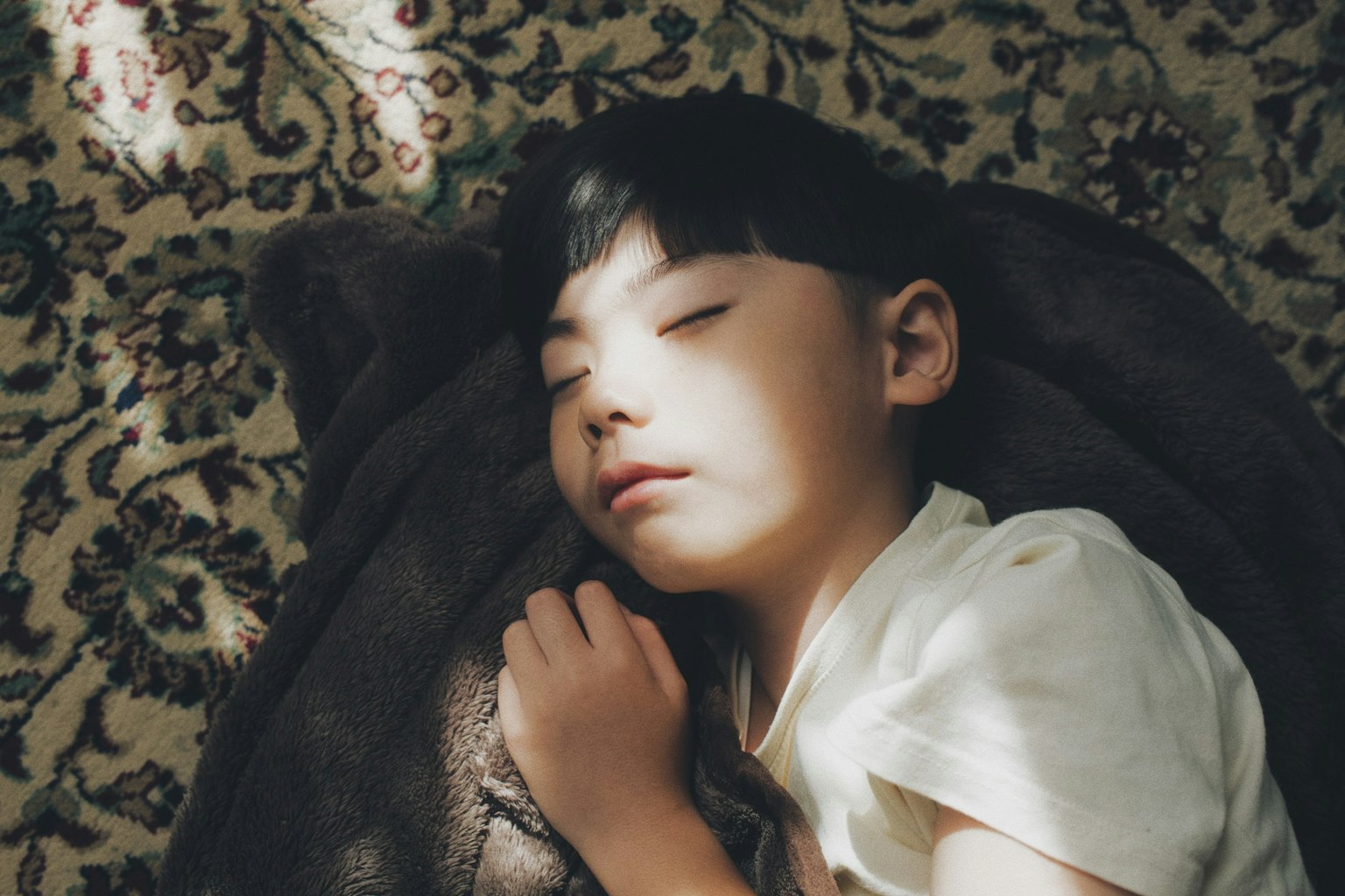 柔らかい毛布の上で眠る子供の横顔 日差しが顔に当たっている