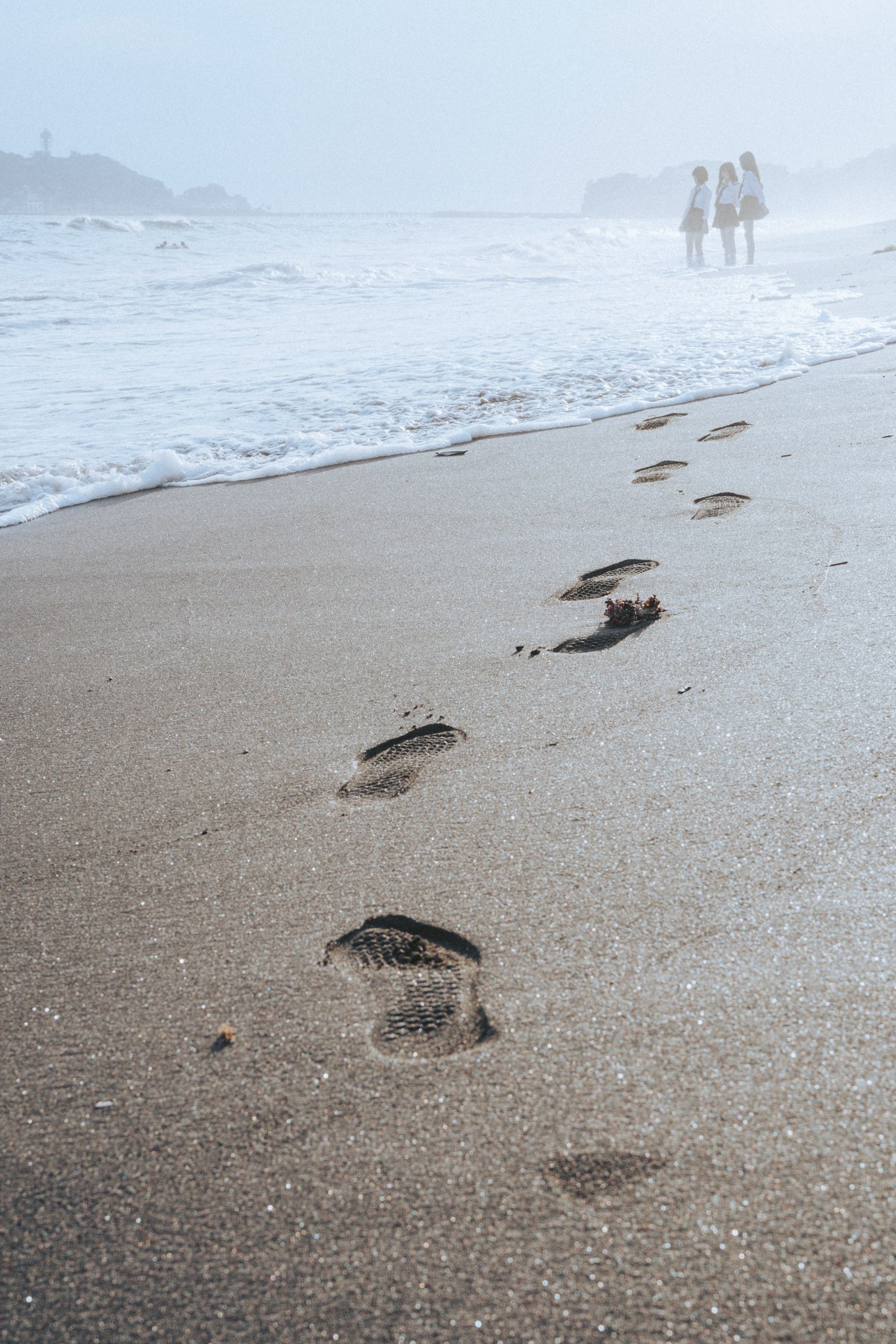 Des empreintes sur une plage de sable avec des personnes dans le brouillard