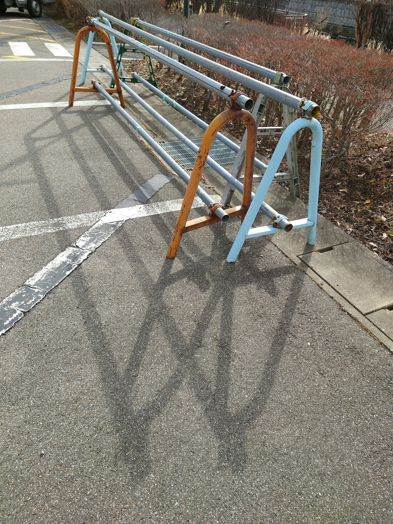 Metal bike rack in blue and orange colors casting shadows on the pavement