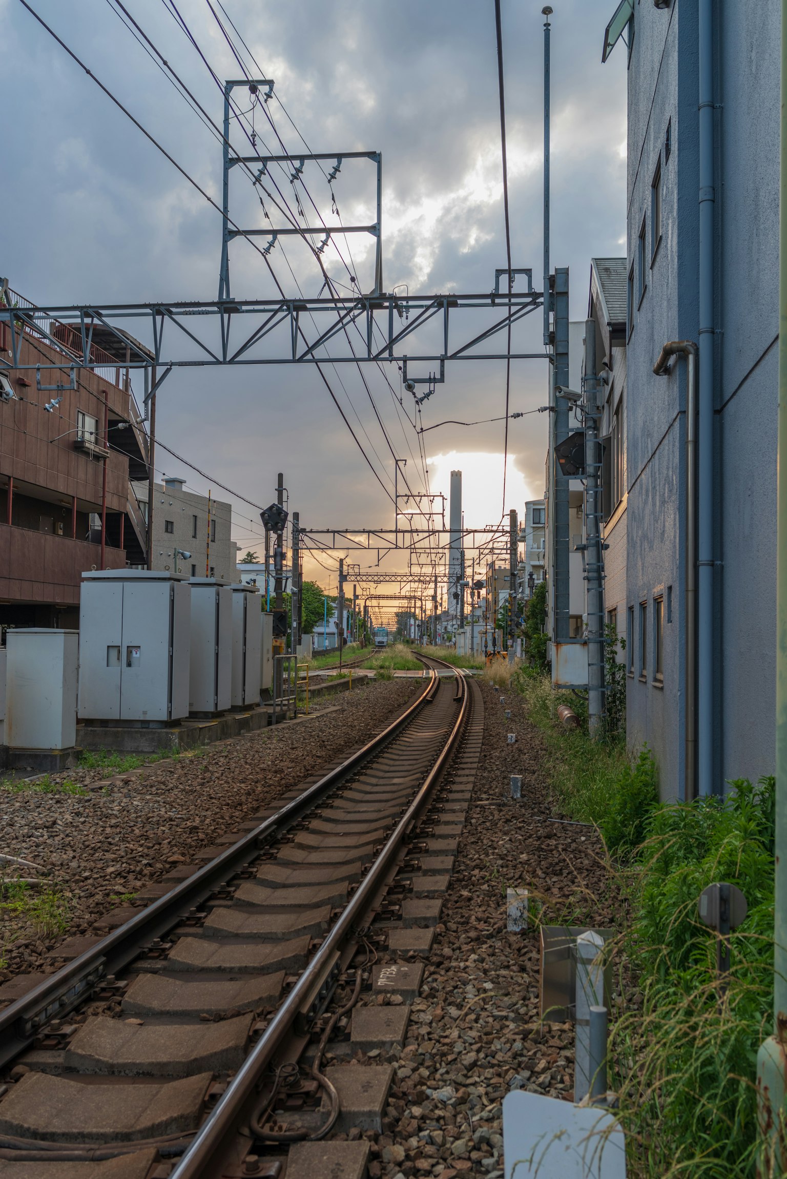 มุมมองของรางรถไฟพร้อมอาคารโดยรอบแสงพระอาทิตย์ตกในพื้นหลัง