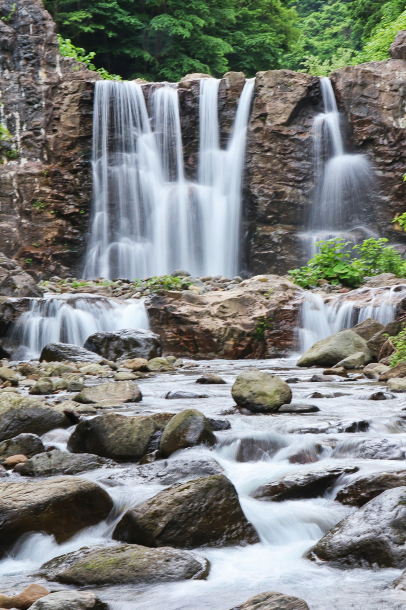 Air terjun yang indah mengalir di atas batu dikelilingi oleh tanaman hijau dan kerikil di sungai