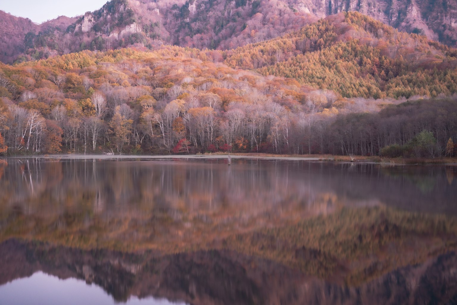 Beautiful autumn landscape with mountains and lake reflection featuring orange and yellow leaves