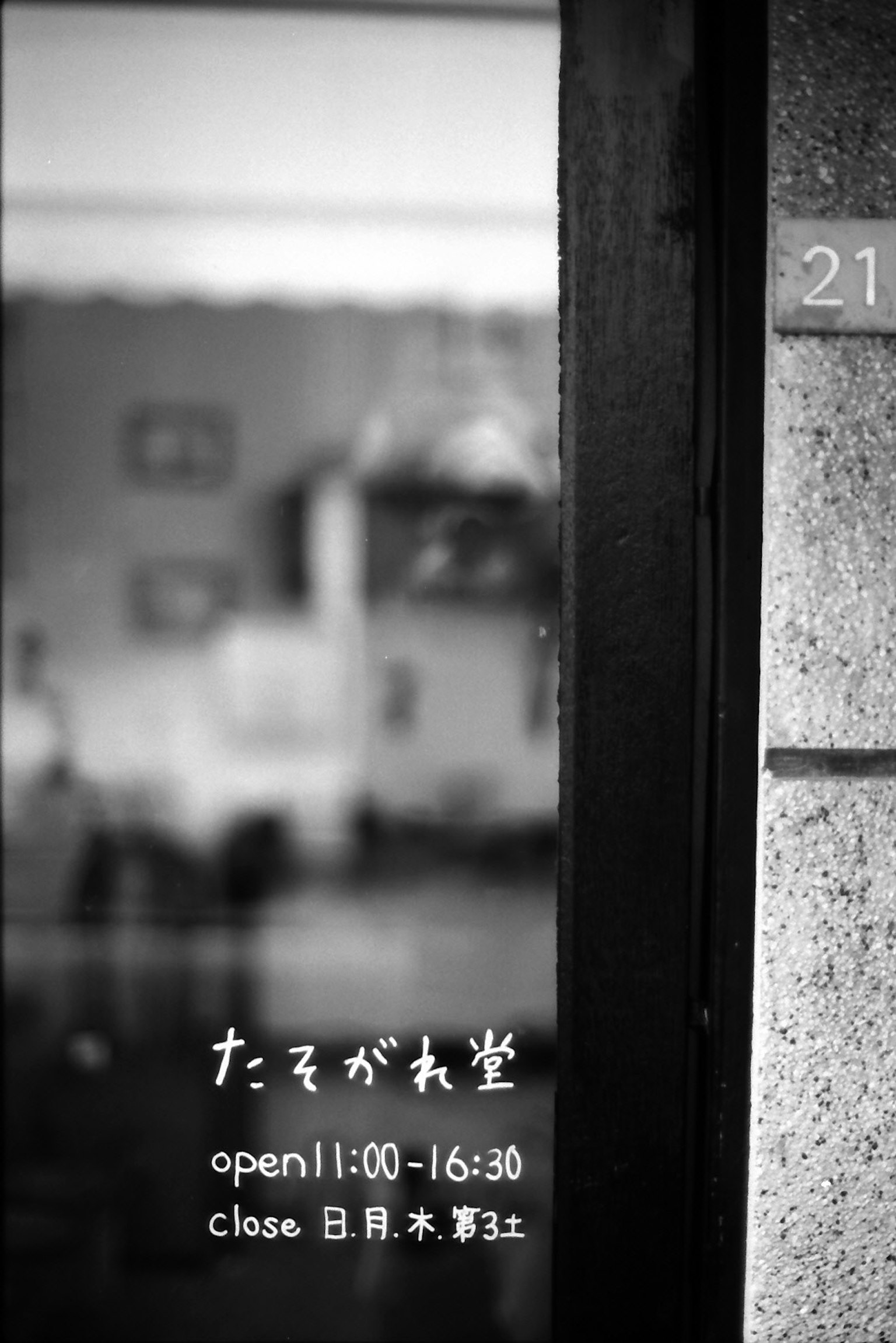 Black and white image of a window with reflections of the interior and a sign showing business hours