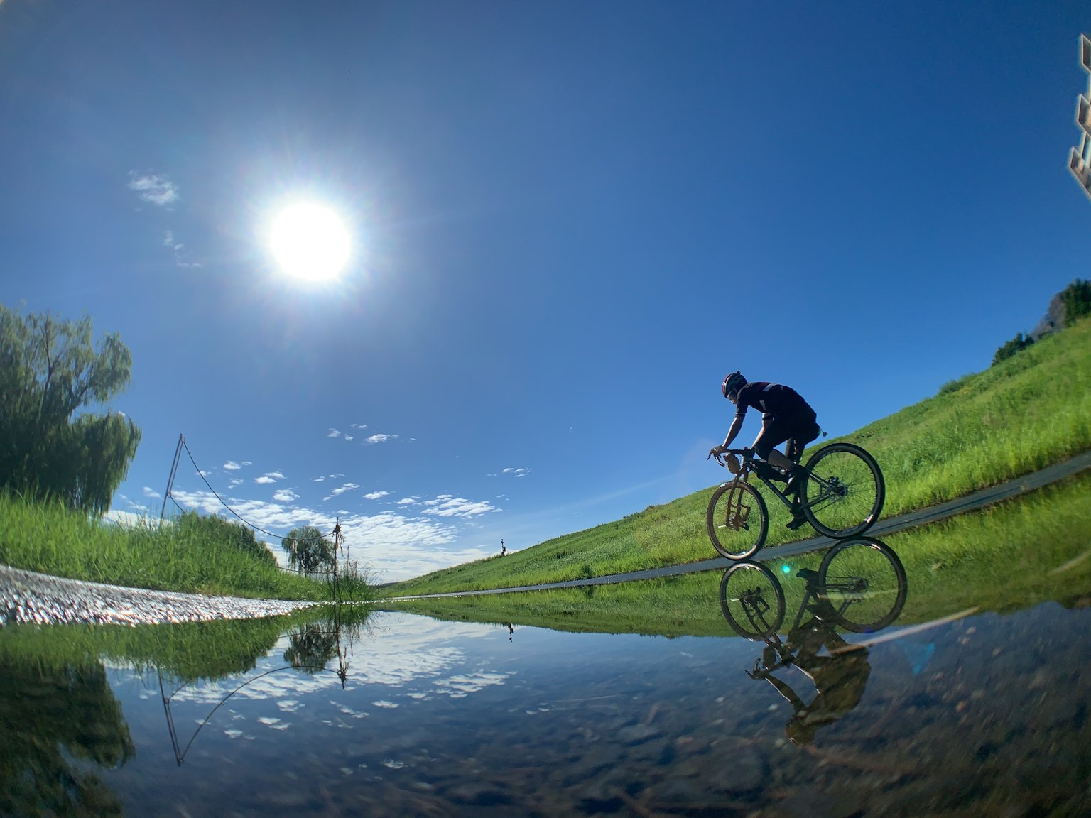Persona in bicicletta sotto un cielo blu con riflesso in una pozzanghera