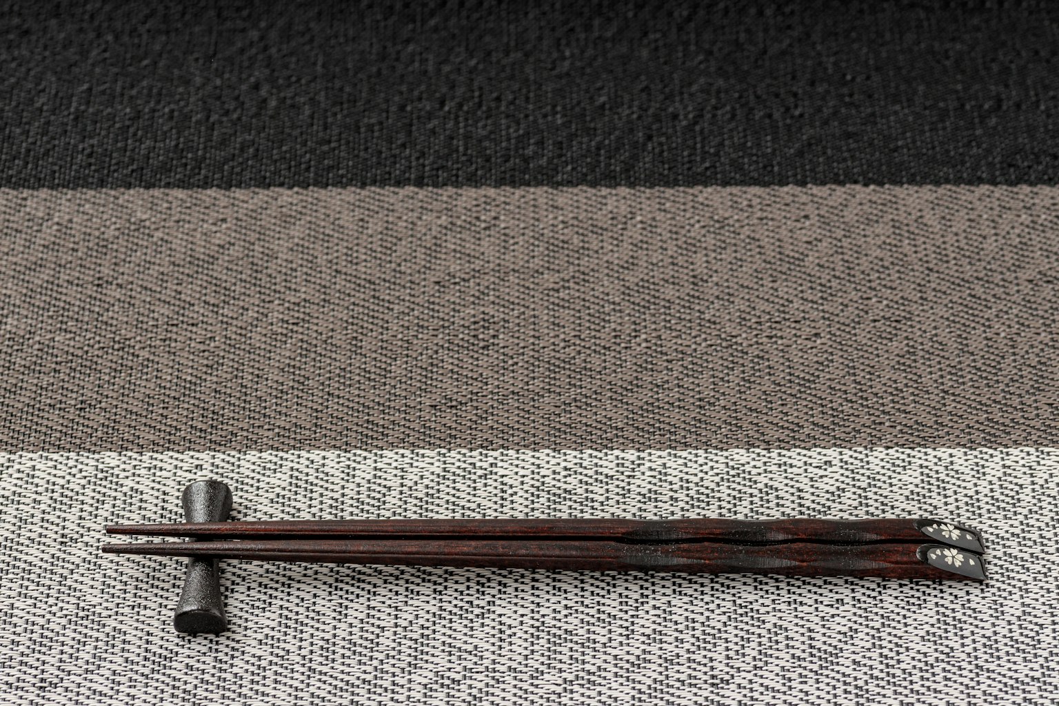 Baguettes en bois et repose-baguettes placés sur un tissu rayé noir, gris et beige