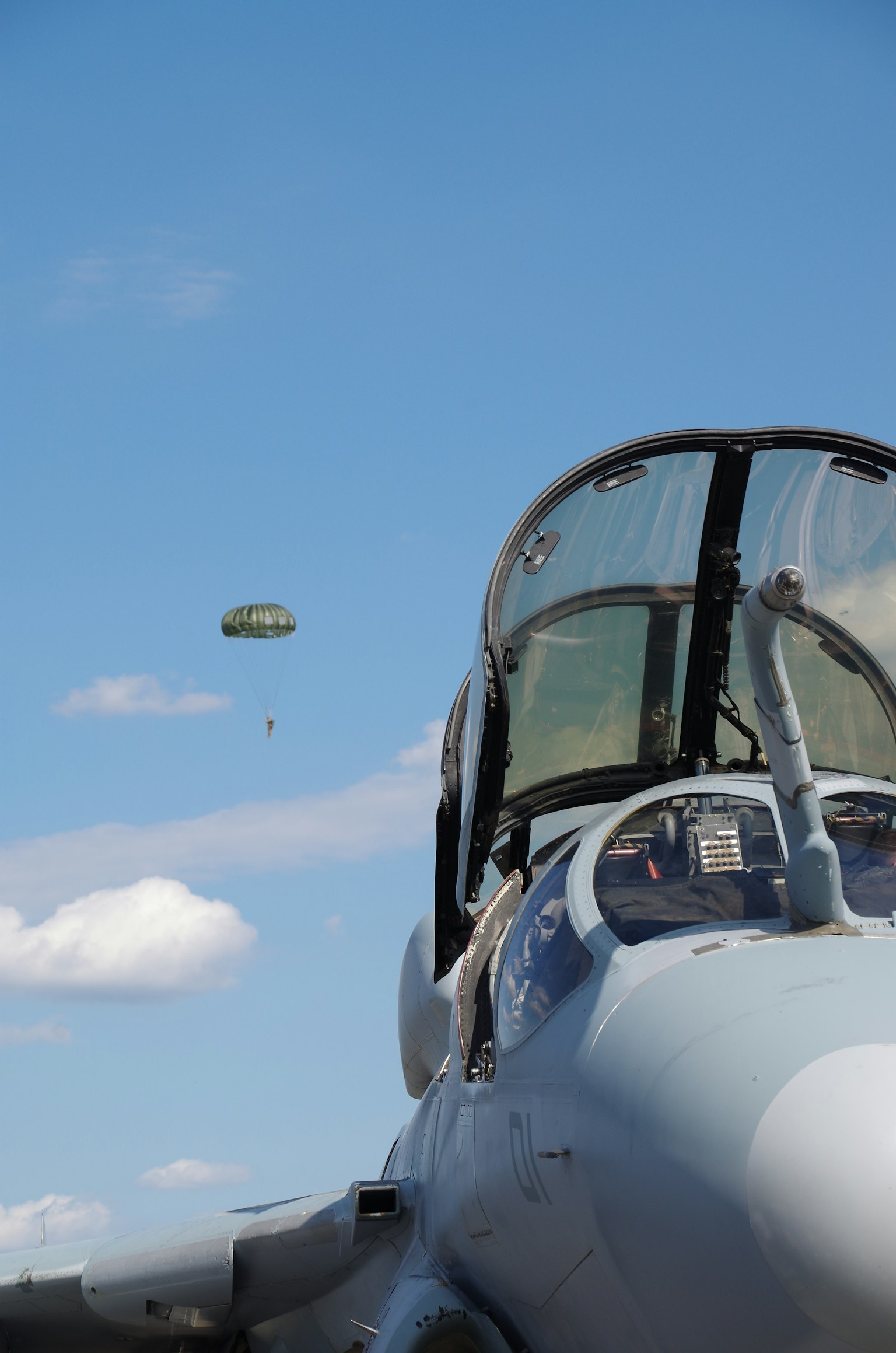 Aereo militare con un paracadute che scende contro un cielo blu