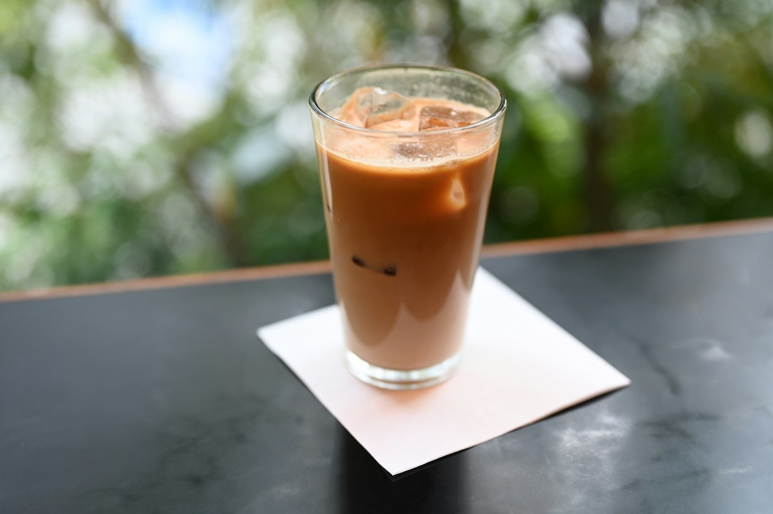 Sebuah gelas transparan berisi kopi es diletakkan di atas meja hitam