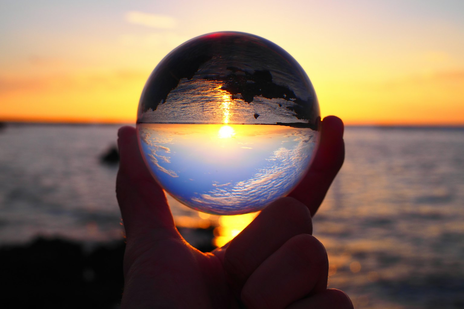 Silhouette di una mano che tiene una sfera di cristallo che riflette il tramonto
