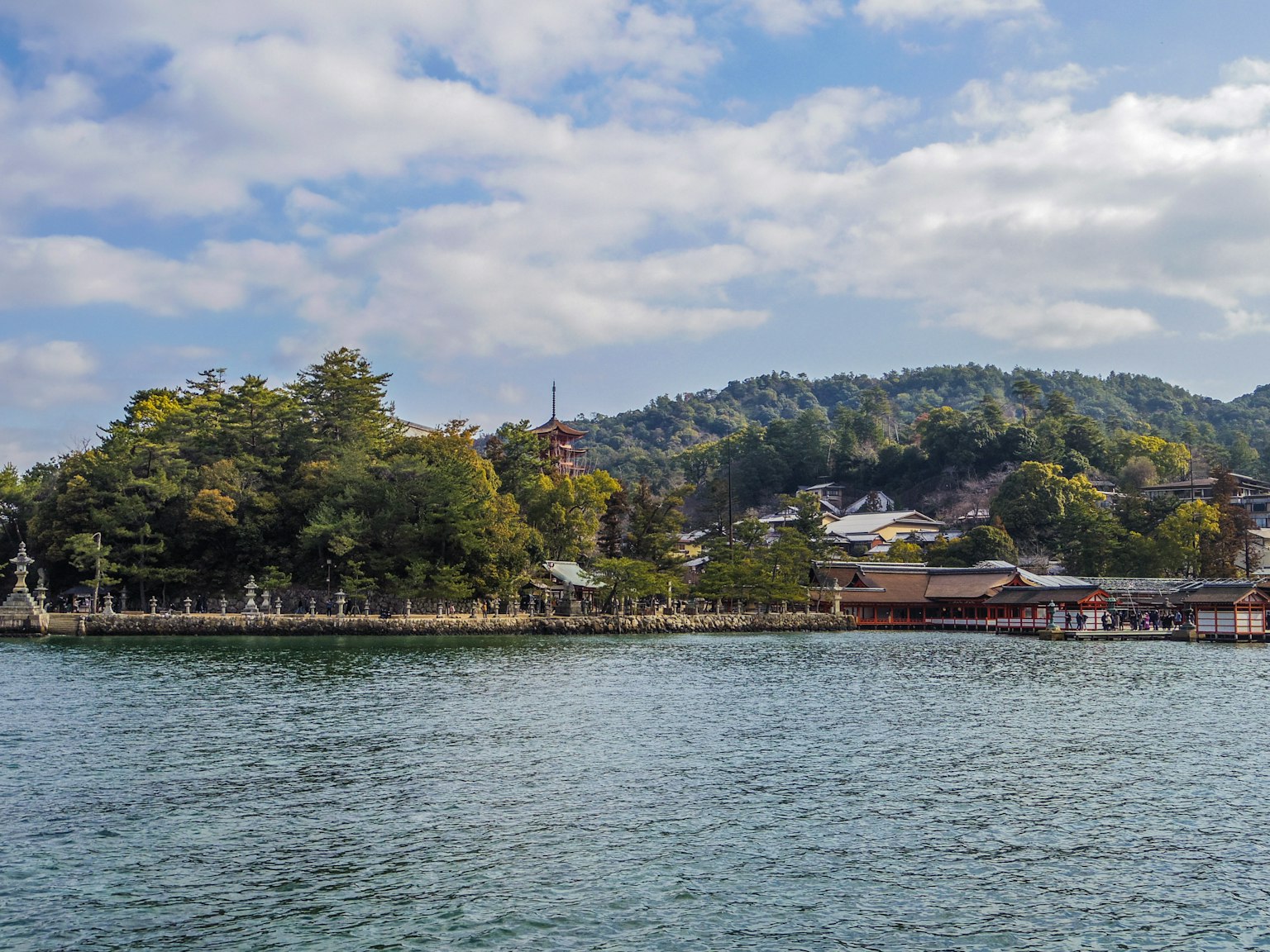 Scenic view of calm waters with lush hills and traditional buildings