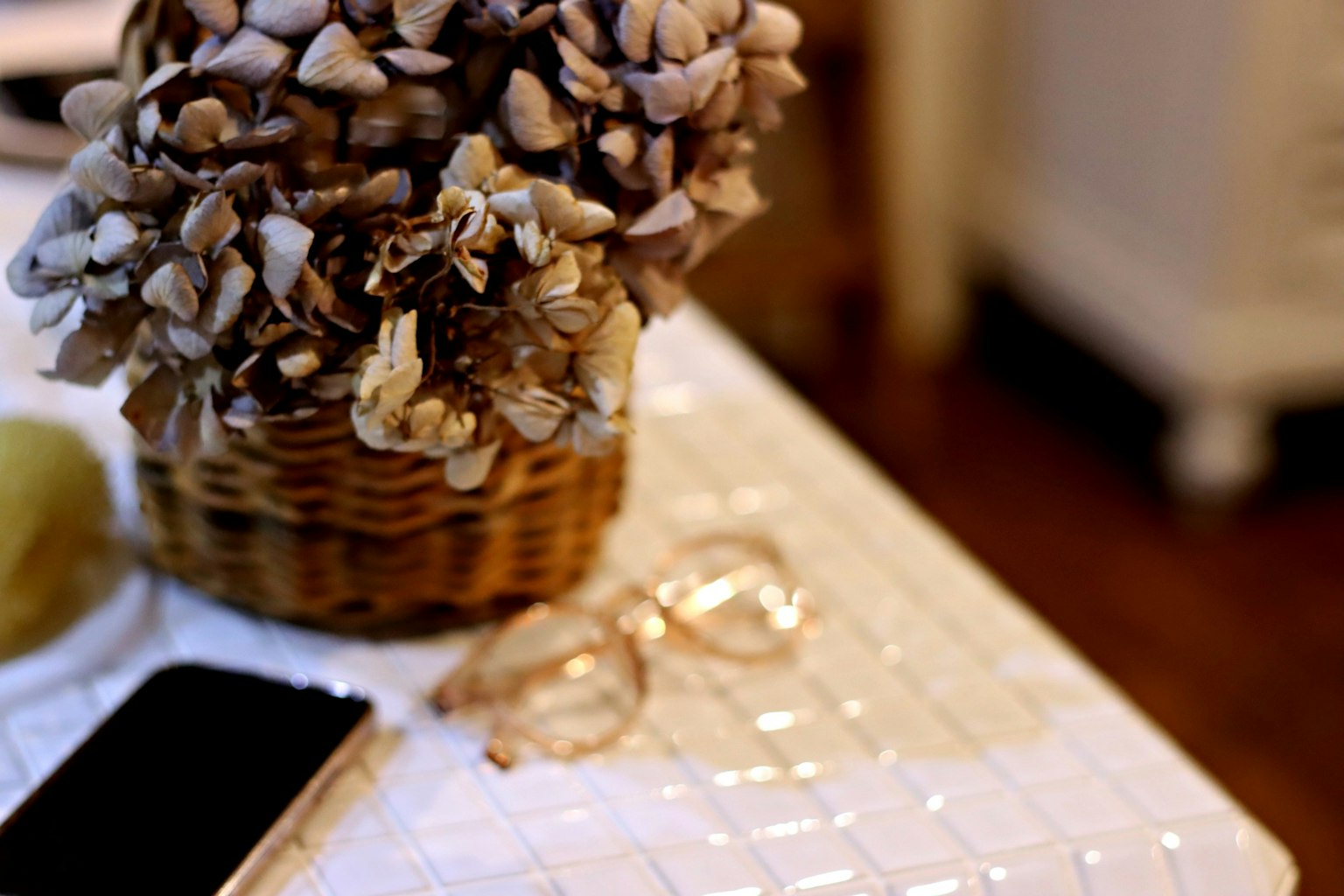 Arreglo floral en una cesta sobre una mesa con gafas y un teléfono