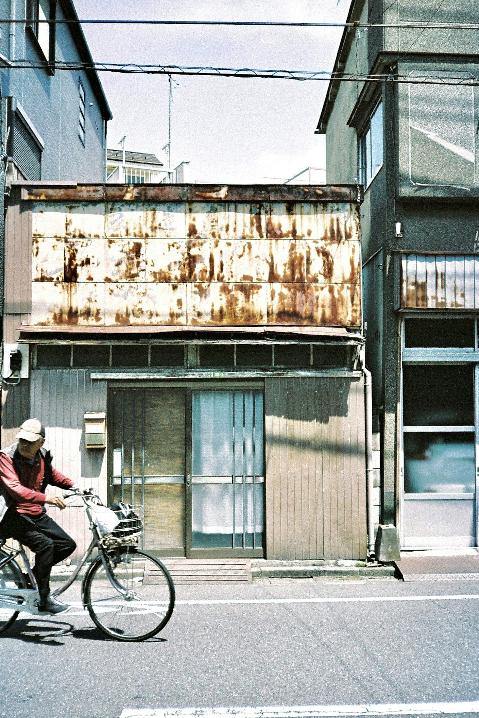 Urban scene featuring a person riding a bicycle in front of a weathered building with a rusty facade