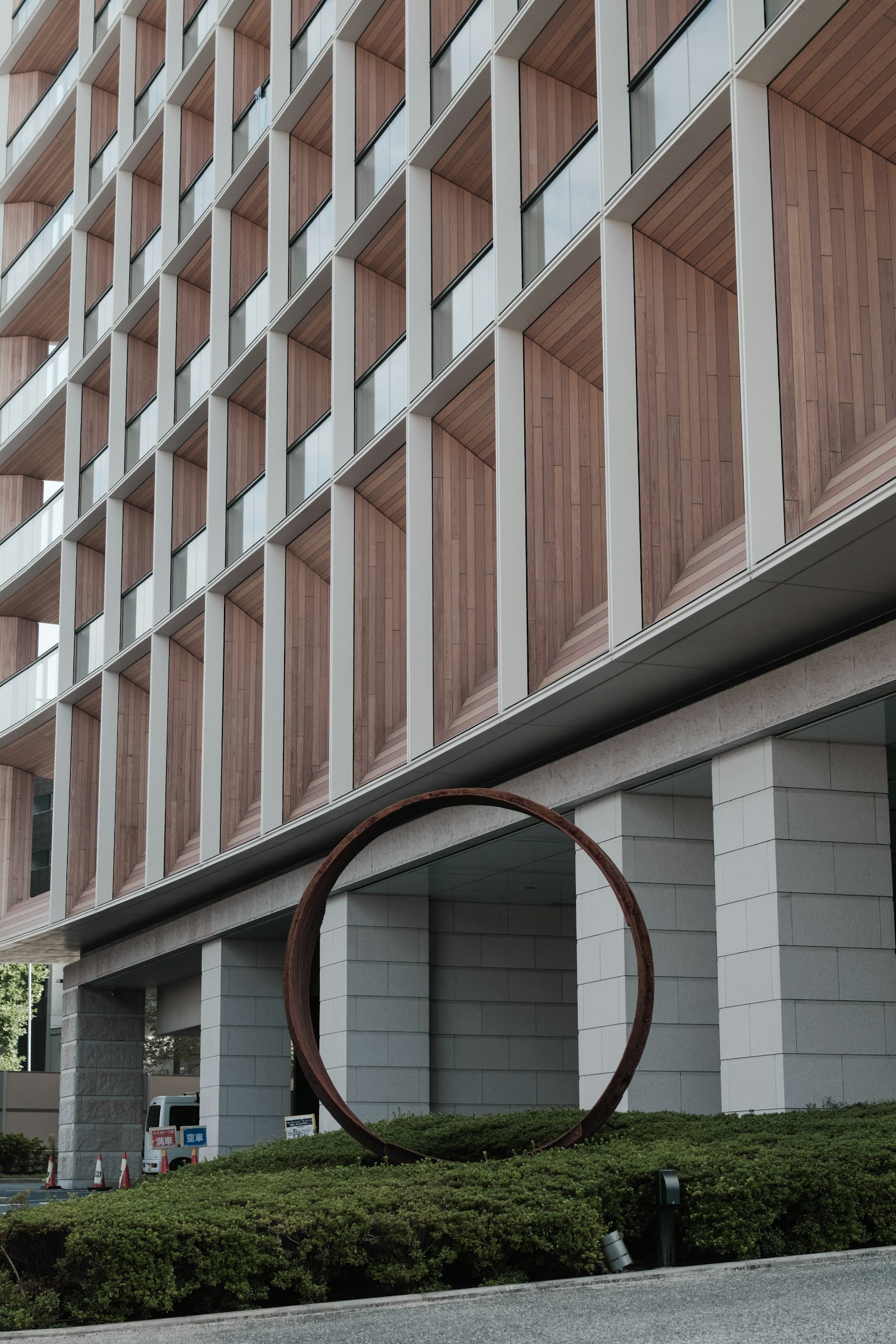 Fachada de edificio moderno con escultura circular y paisajismo verde