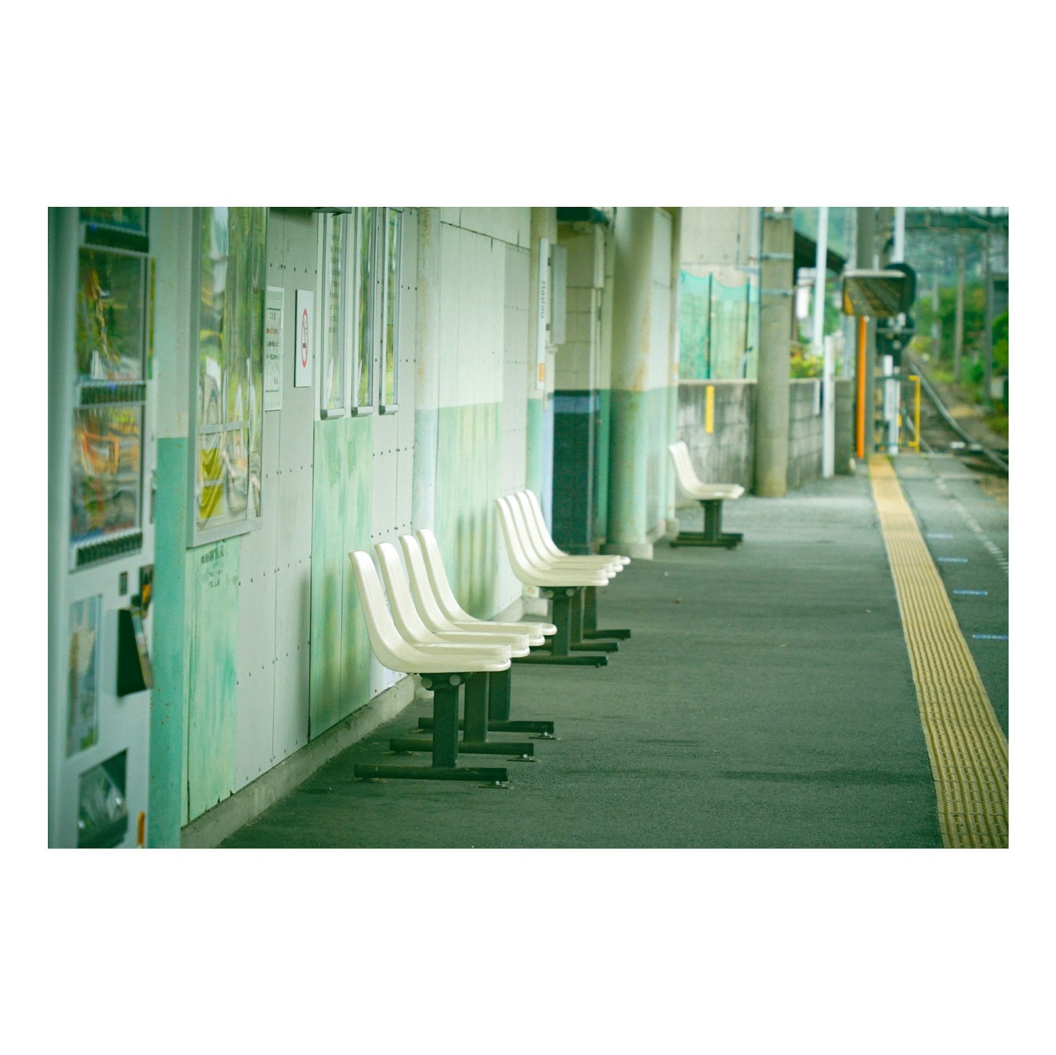 駅のプラットフォームに並ぶ白い椅子と緑の壁