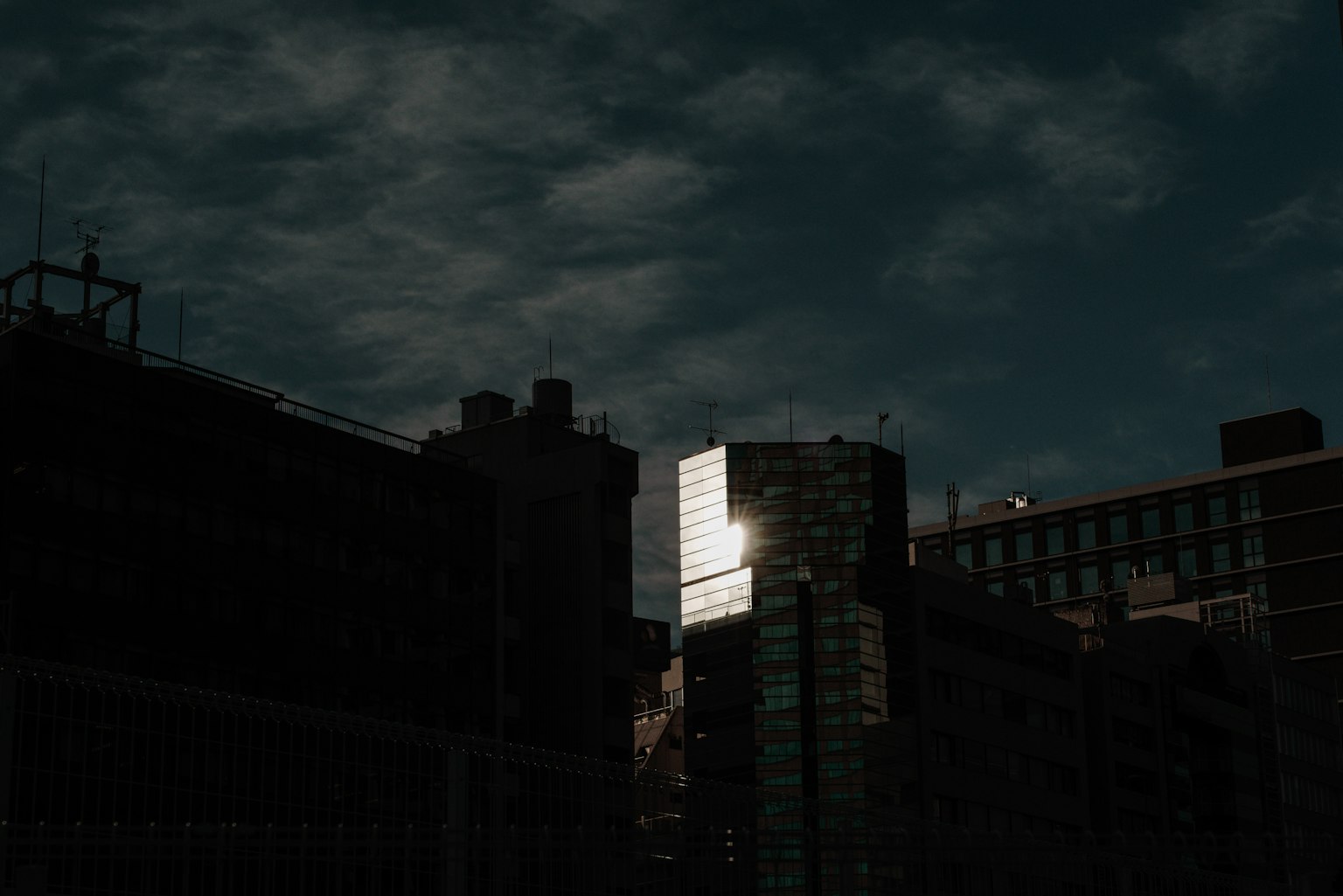 Silhouettierte Gebäude vor einem dunklen Himmel mit hellem Reflex auf Glas