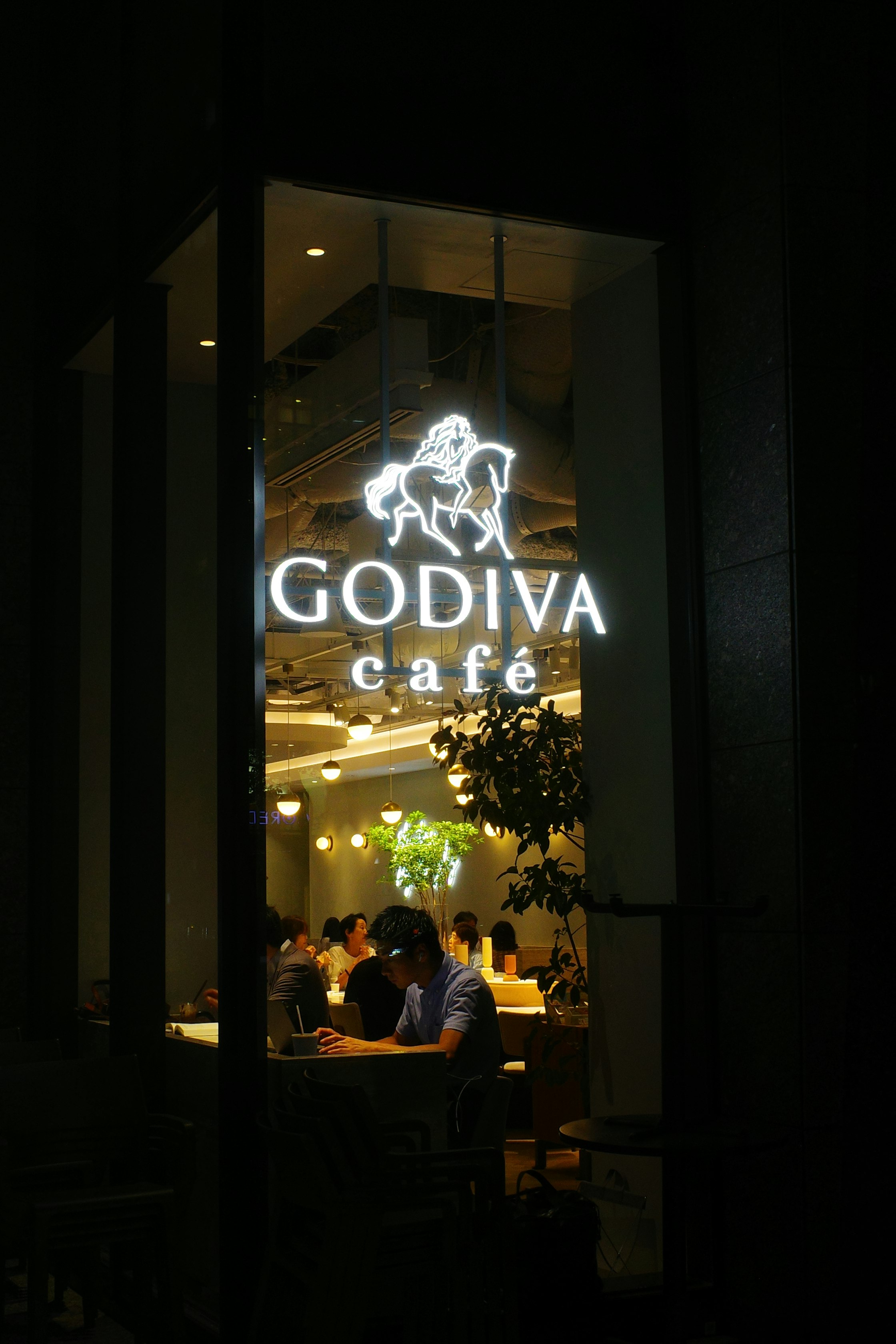 夜の店内窓越しに見える「GODIVA cafe」のネオン看板と人々