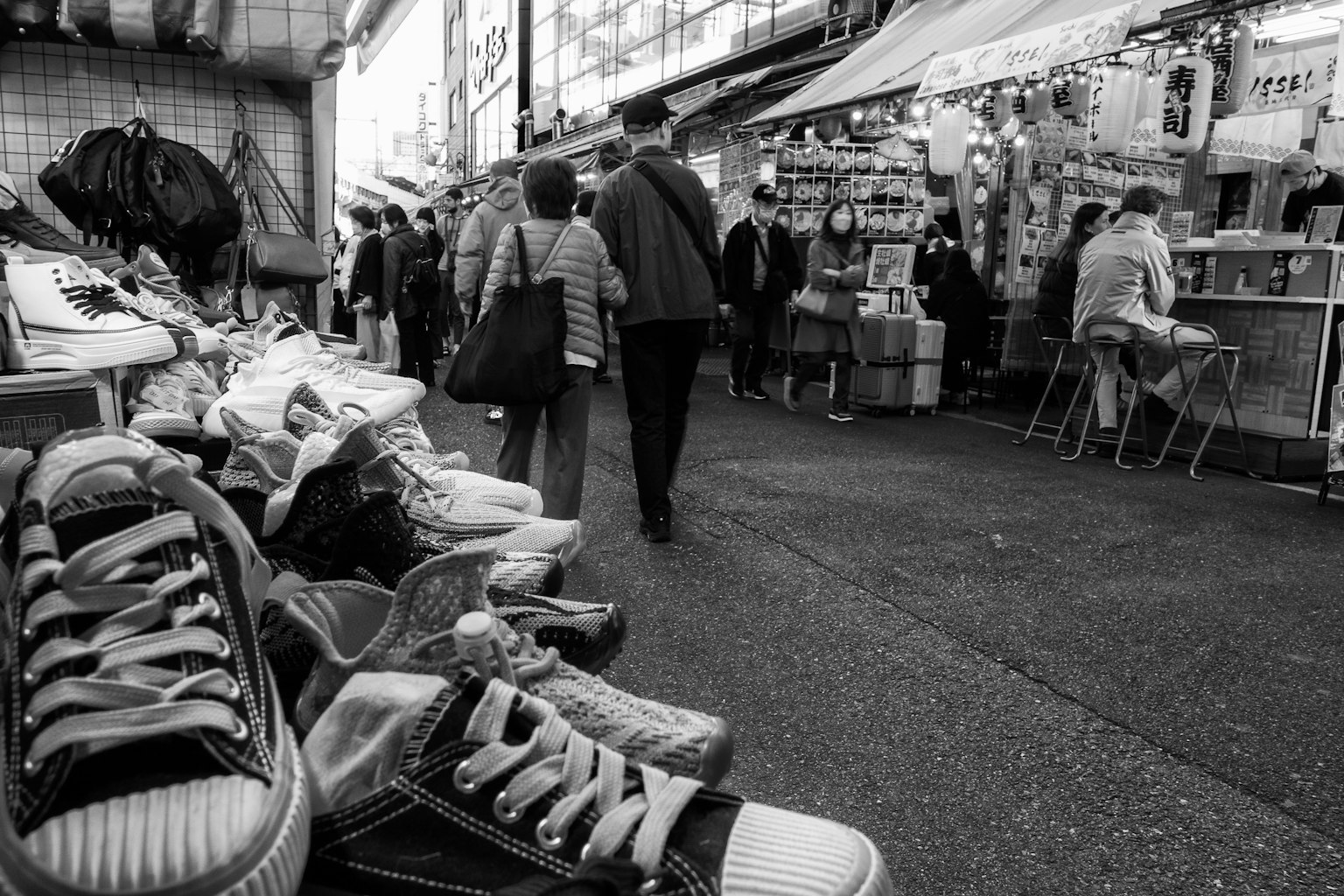 Escena de mercado en blanco y negro con zapatos en primer plano y personas caminando