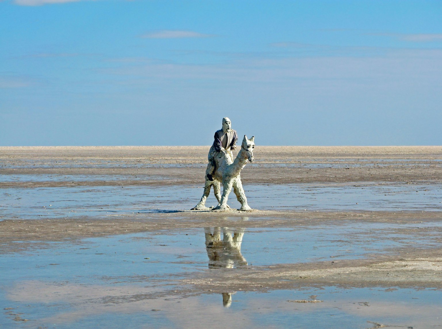 Une personne montée sur un cheval marchant à travers un marais salé sous un ciel bleu