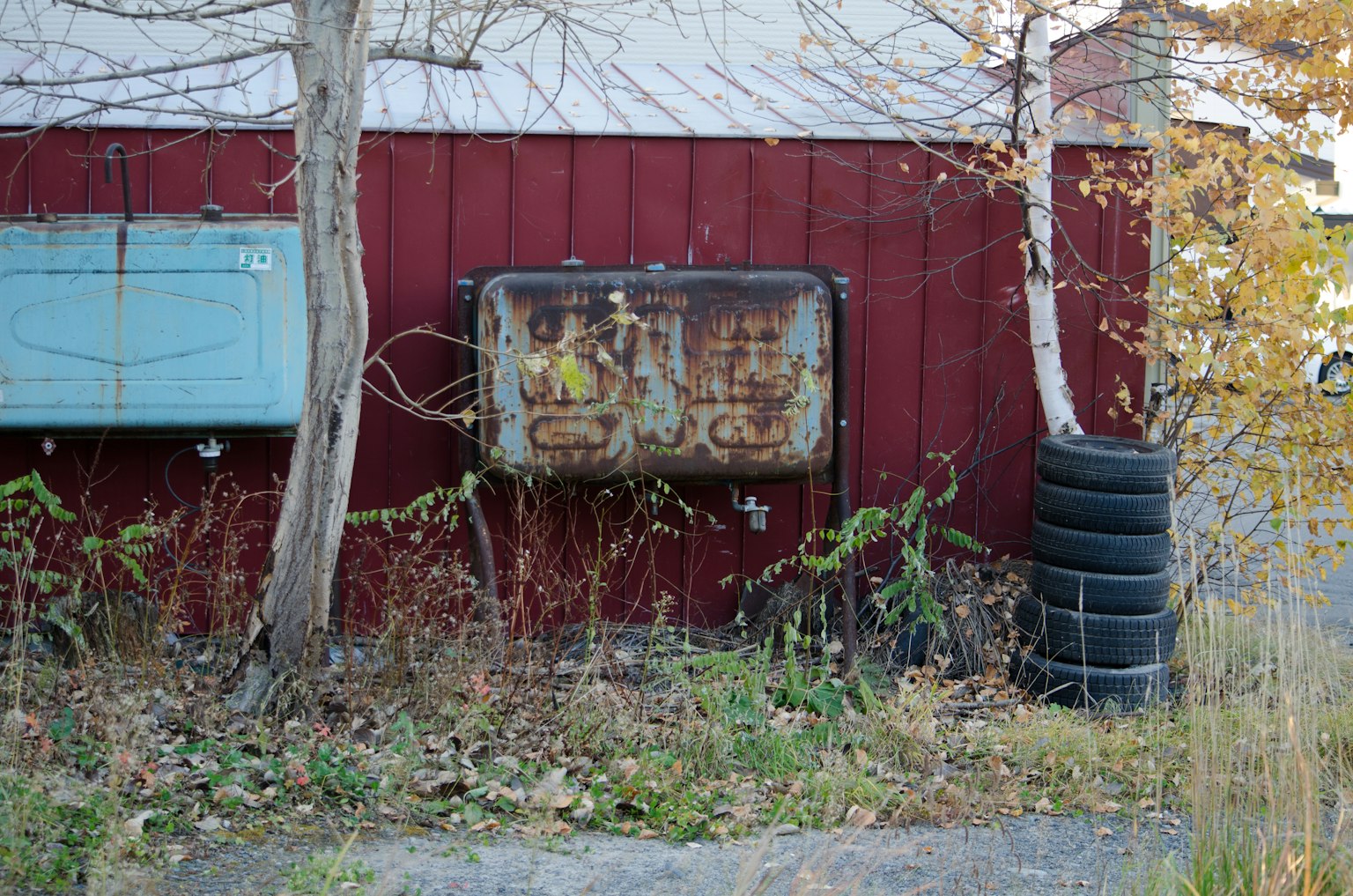 Old gas pump against a red wall with weeds and tires nearby