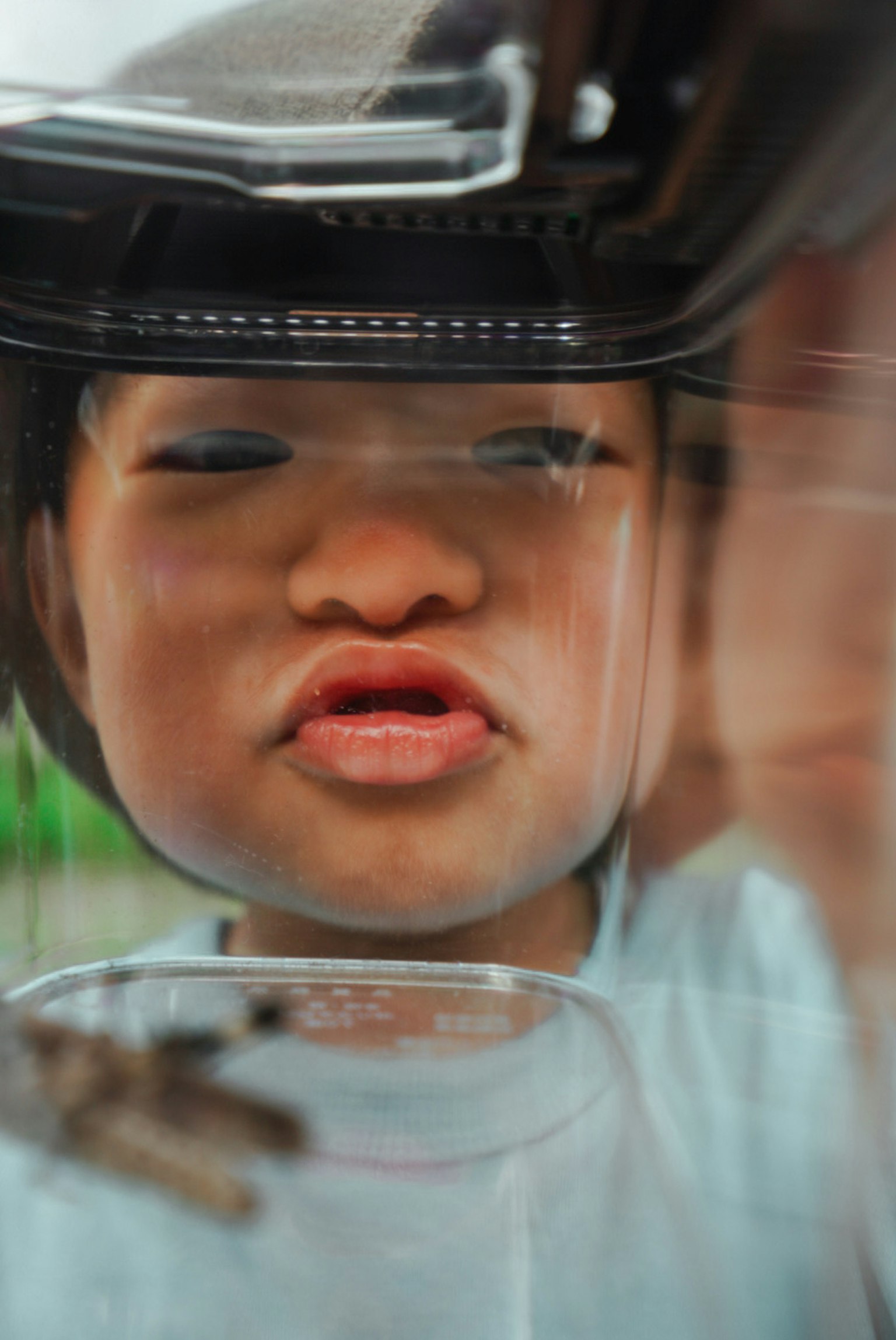 Volto di un bambino che guarda attraverso un contenitore trasparente con un'espressione curiosa