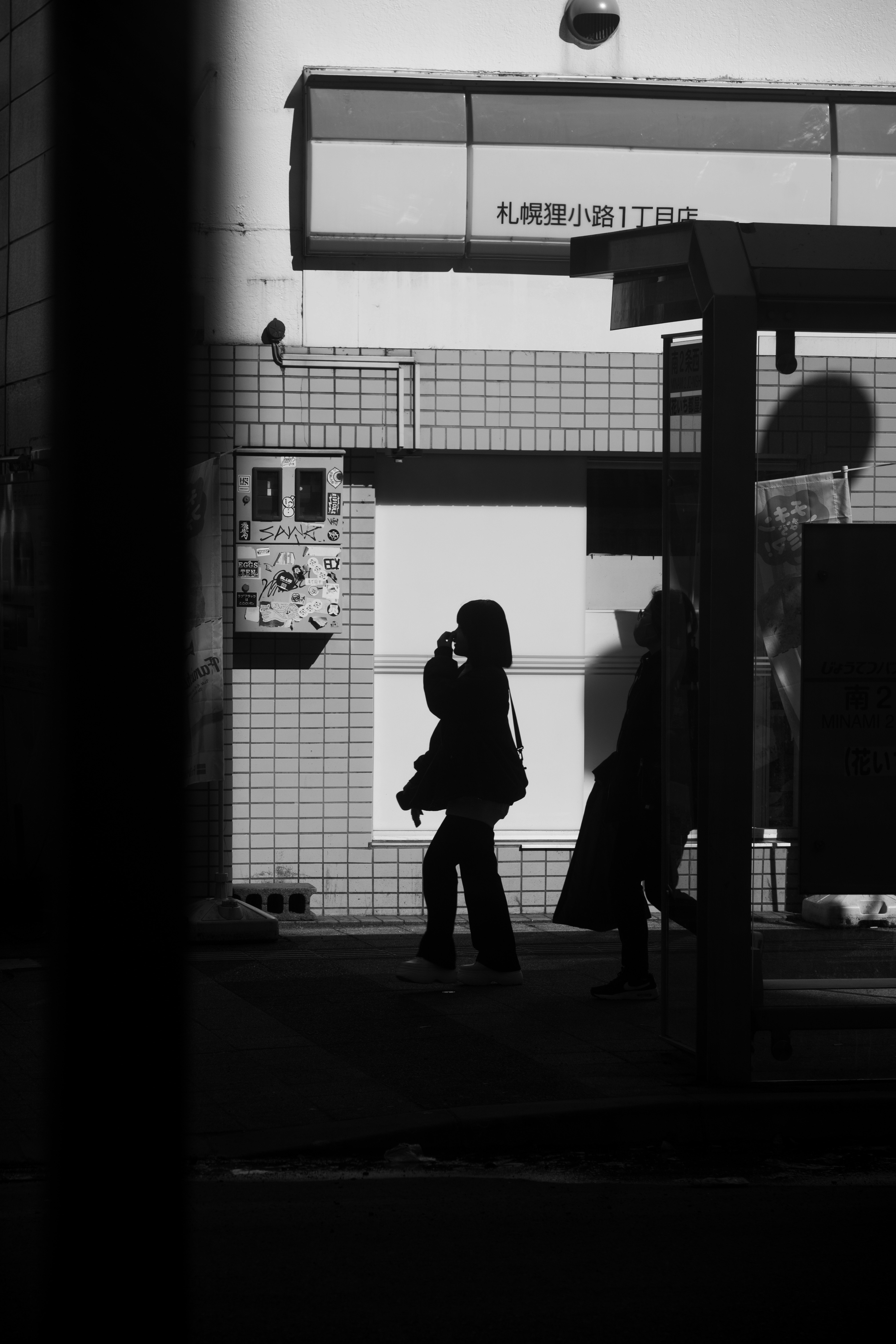 白黒の街角で電話をかける女性のシルエットと影