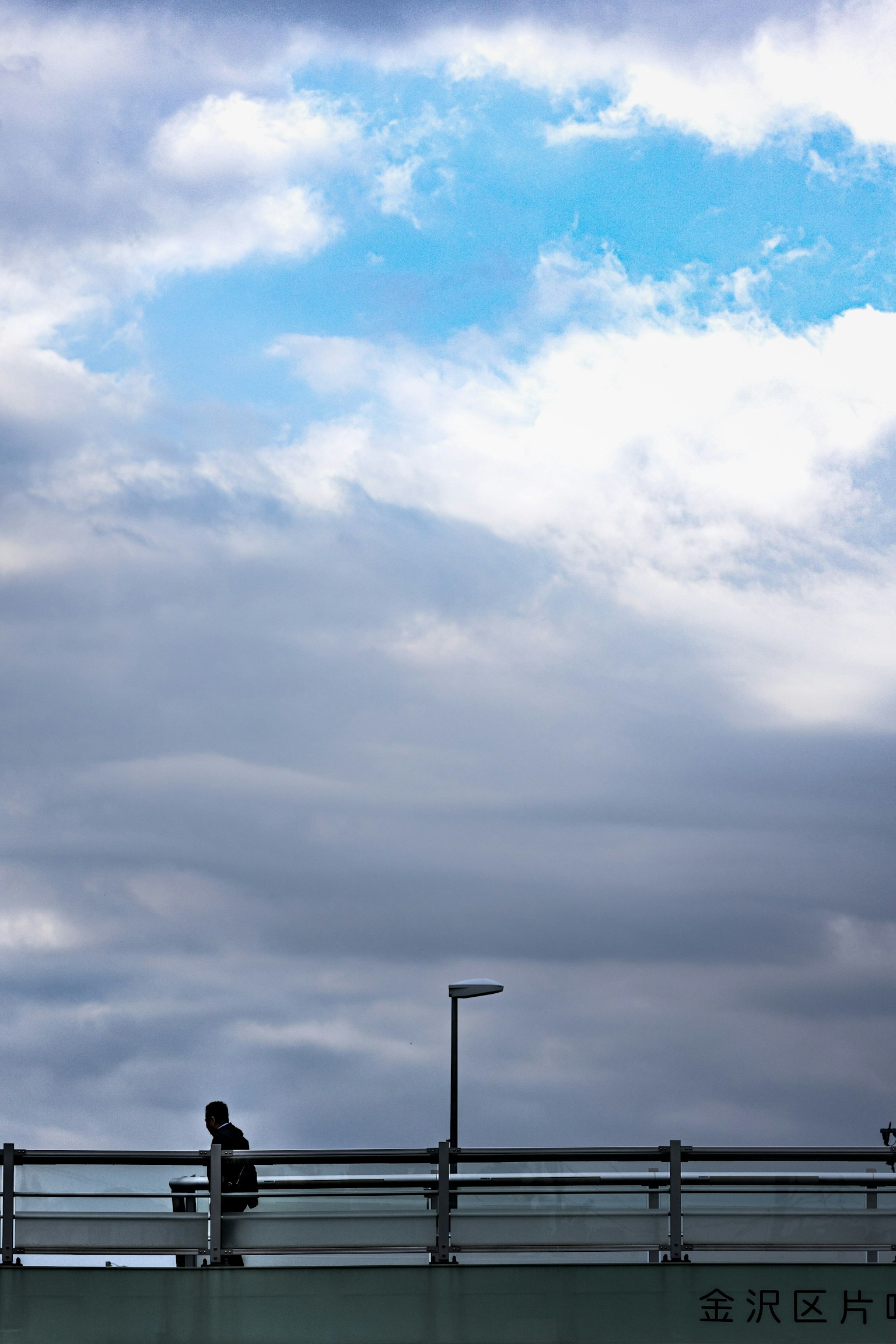 Eine Person, die auf einer Brücke unter einem blauen Himmel mit Wolken geht