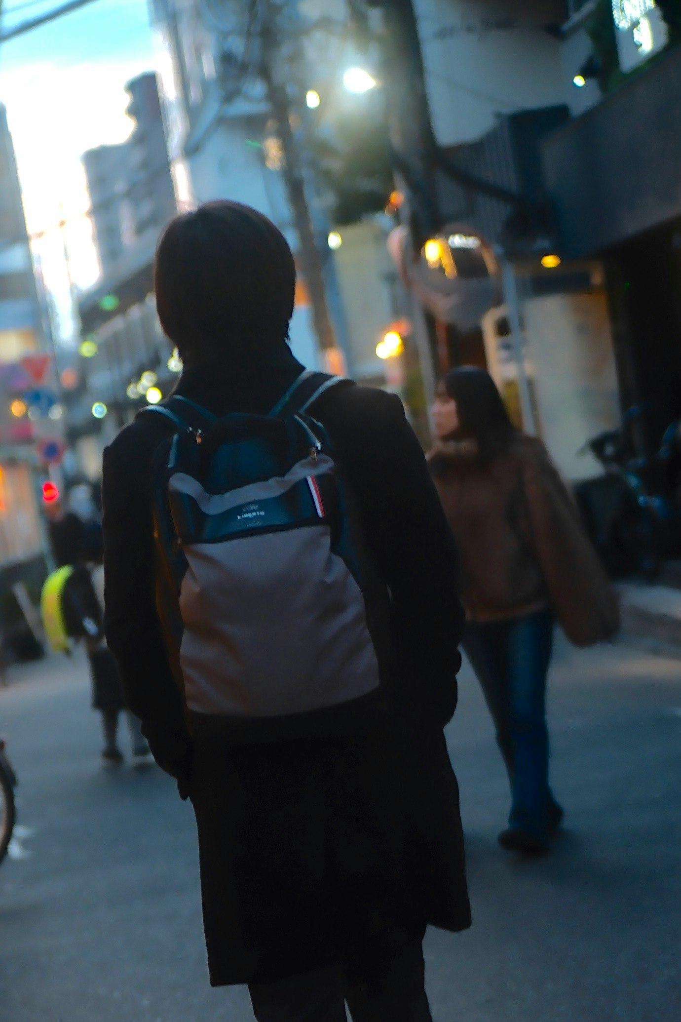 夜の街でリュックを背負って歩く人々の後ろ姿