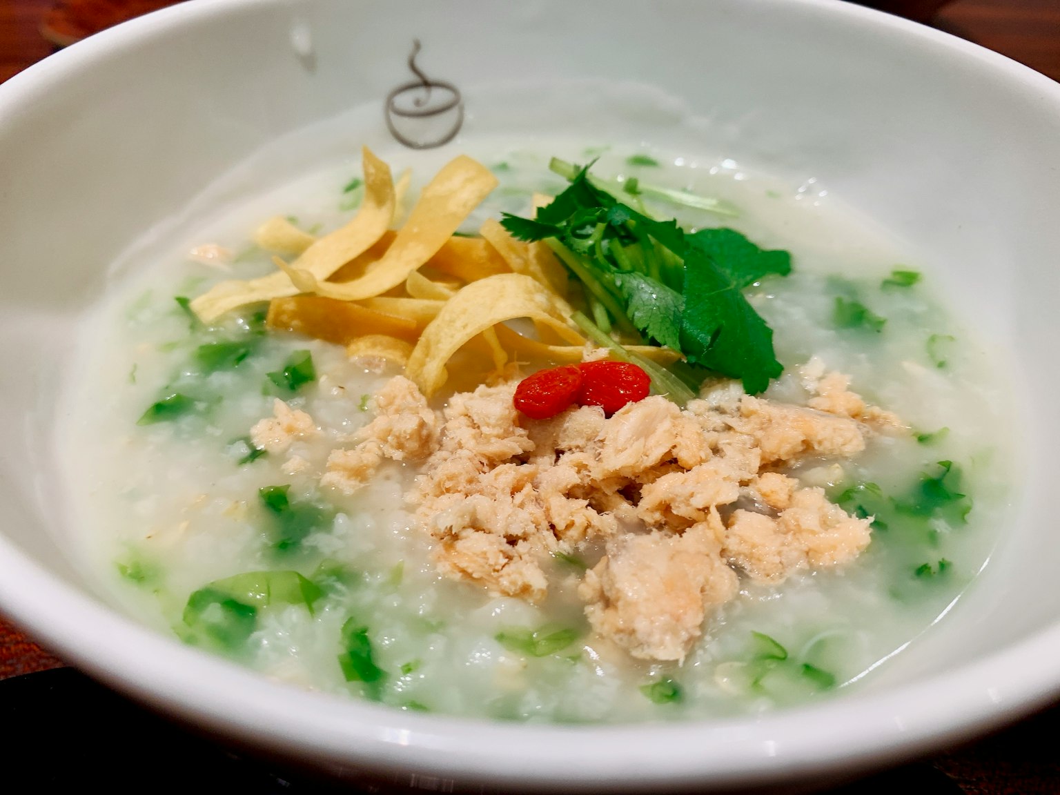 Una ciotola di porridge di riso guarnita con pollo sfilacciato, strisce d'uovo e coriandolo