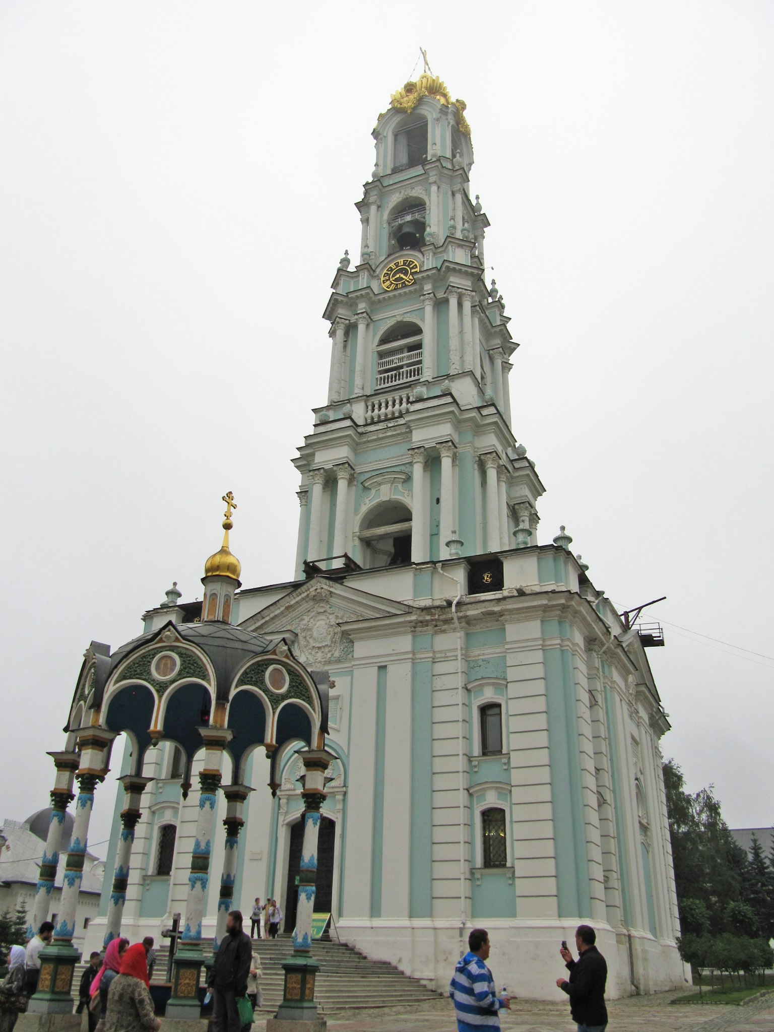 Exterior view of a church featuring a tall tower and golden domes People walking around the structure