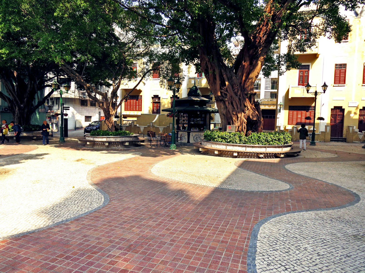 Une grande place avec un arbre central entouré de bancs et de bâtiments