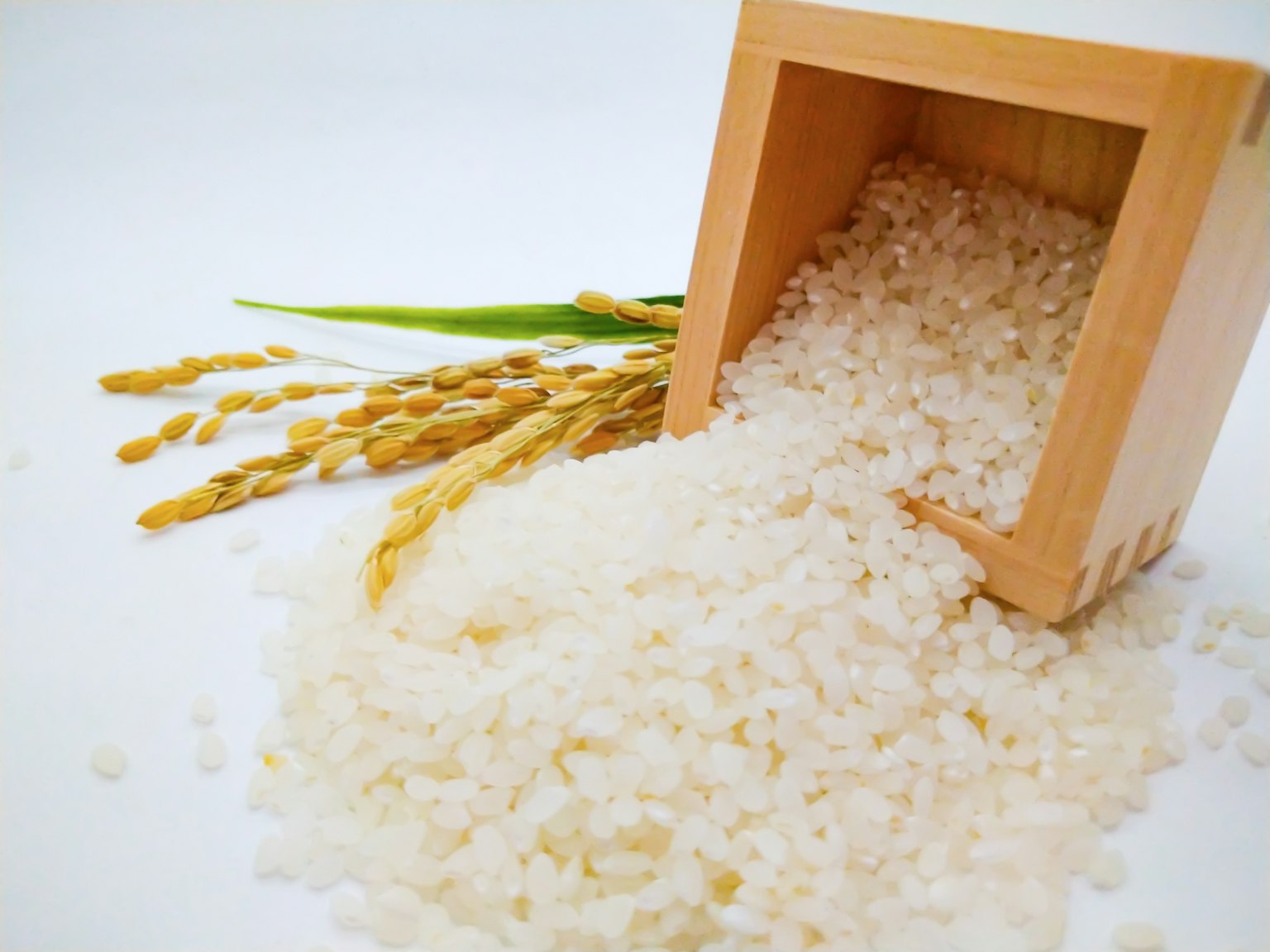 Riso bianco che fuoriesce da un contenitore di legno con spighe di riso