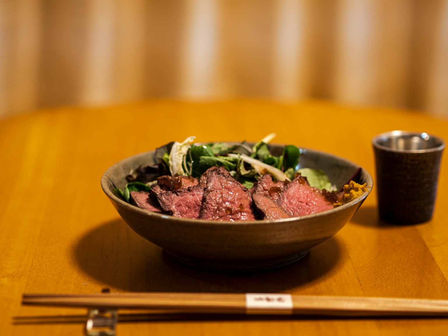 Piatto giapponese splendidamente disposto con carne affettata servita con insalata in una ciotola accanto a bacchette sul tavolo