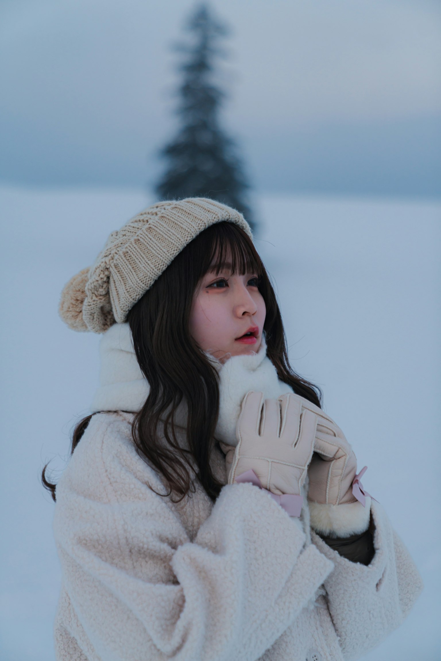 눈 속에서 흰 코트와 니트 모자를 쓴 여성이 손을 따뜻하게 하고 있다