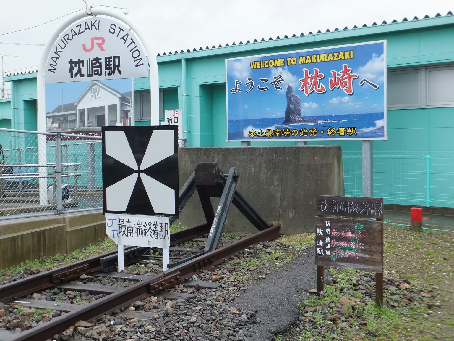 Vista del cartello della stazione di Hamazaki e dei binari con una pubblicità