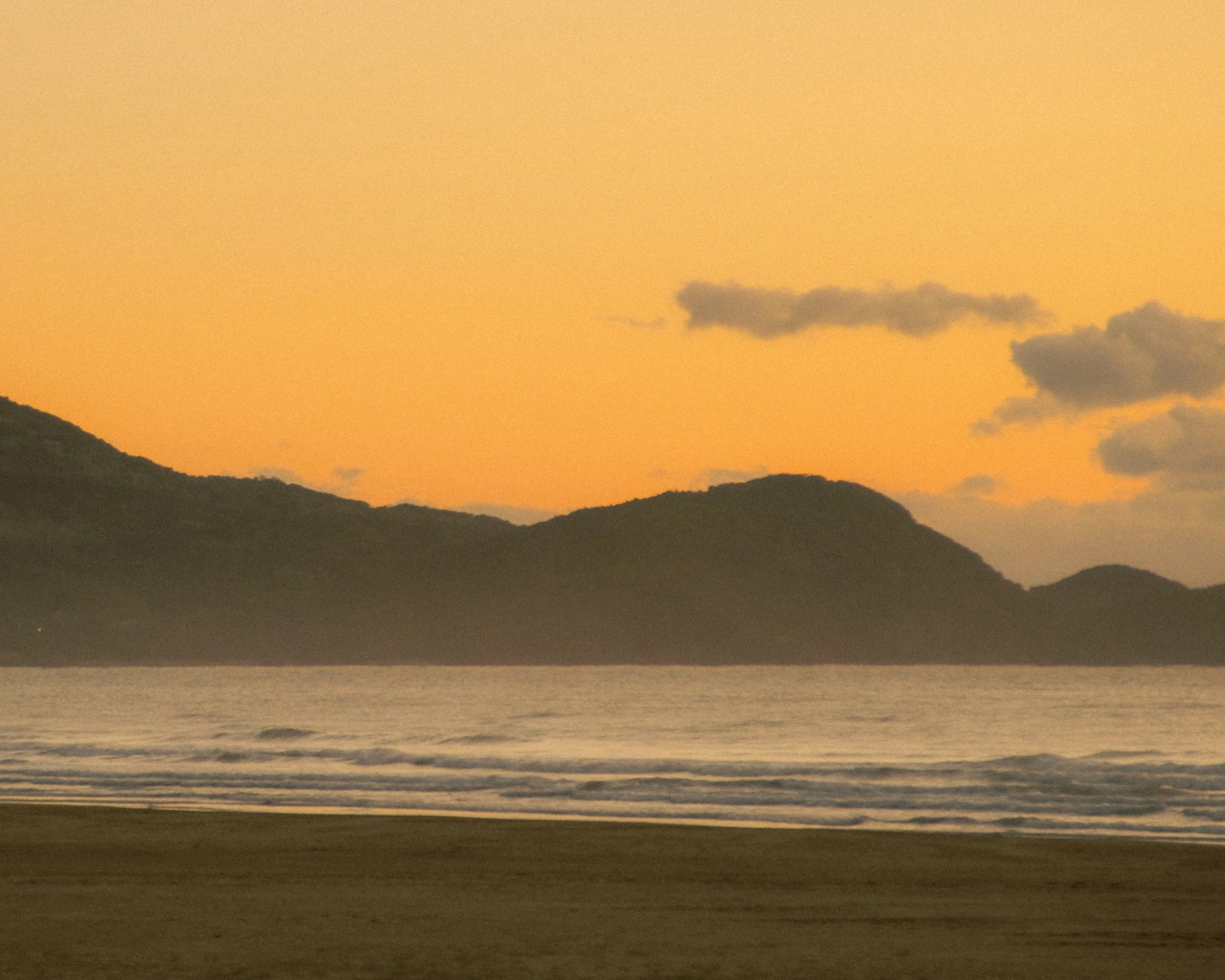 Pemandangan pantai yang indah saat matahari terbenam dengan ombak lembut dan gunung di kejauhan