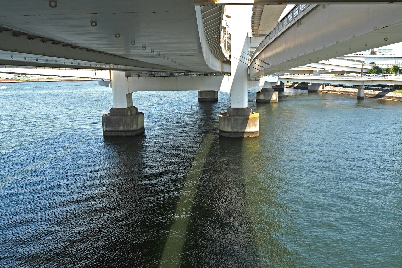 Pemandangan di bawah jembatan menunjukkan pilar penyangga dan pantulan di air