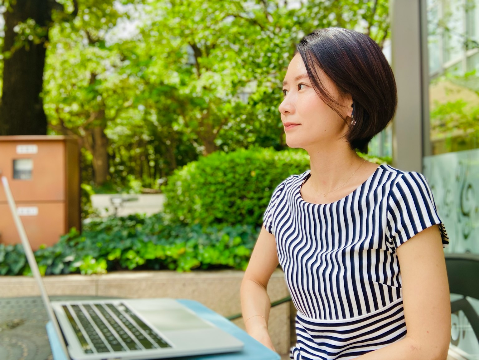 Seitenansicht einer Frau, die in einer grünen Außenumgebung einen Laptop benutzt