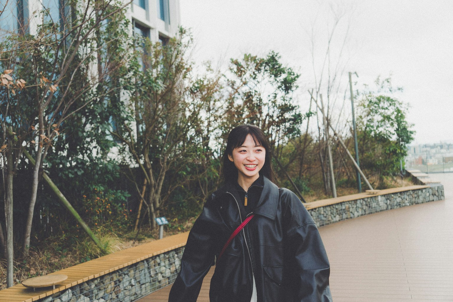 微笑的年輕女性在公園裡走路，潮濕的地面和綠色的樹木