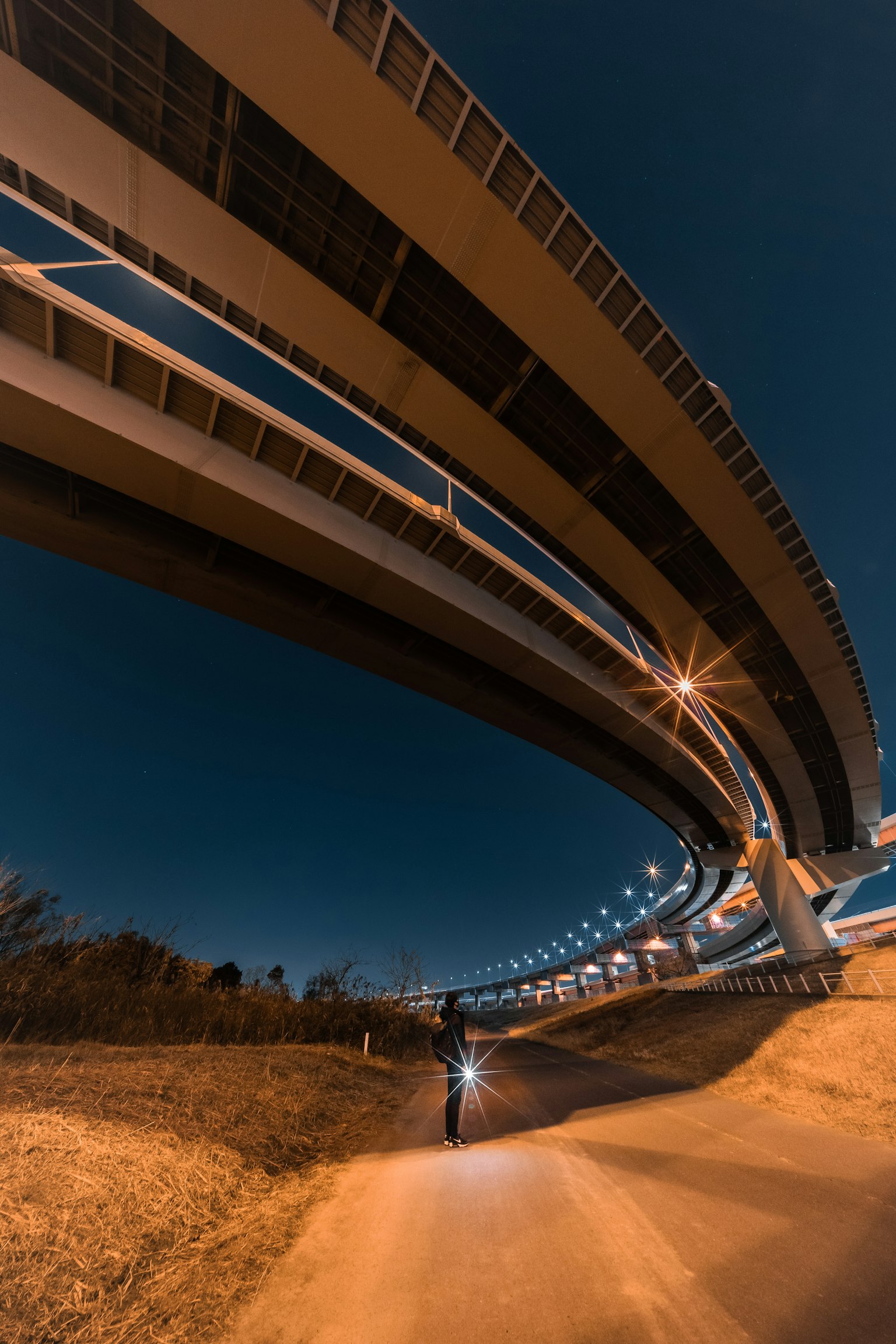 Bogenförmige Autobahnstruktur von unten bei Nacht mit einem Radfahrer gesehen