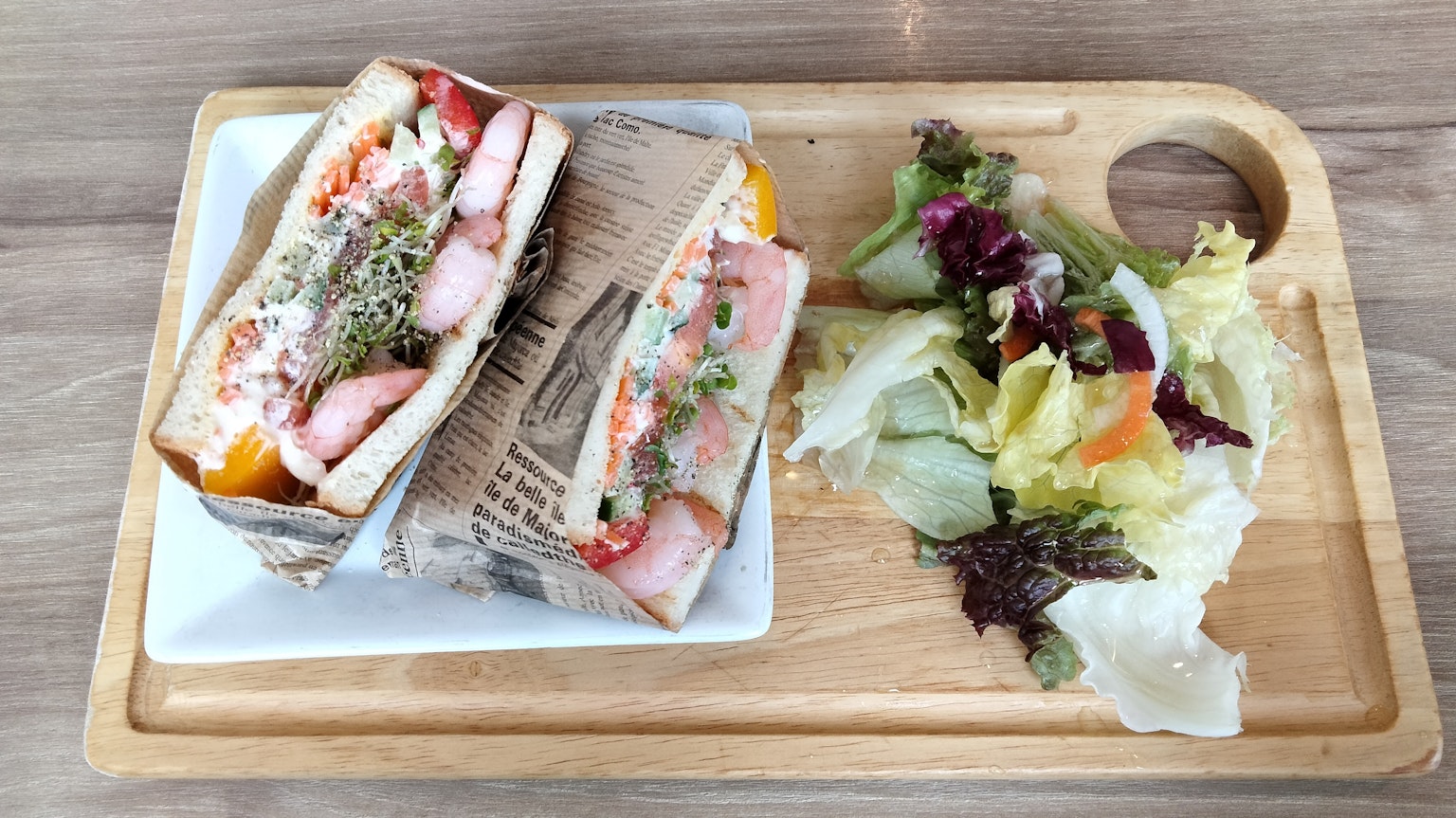 Zwei Sandwiches mit frischen Zutaten auf einem Holztablett neben einem bunten Salat serviert