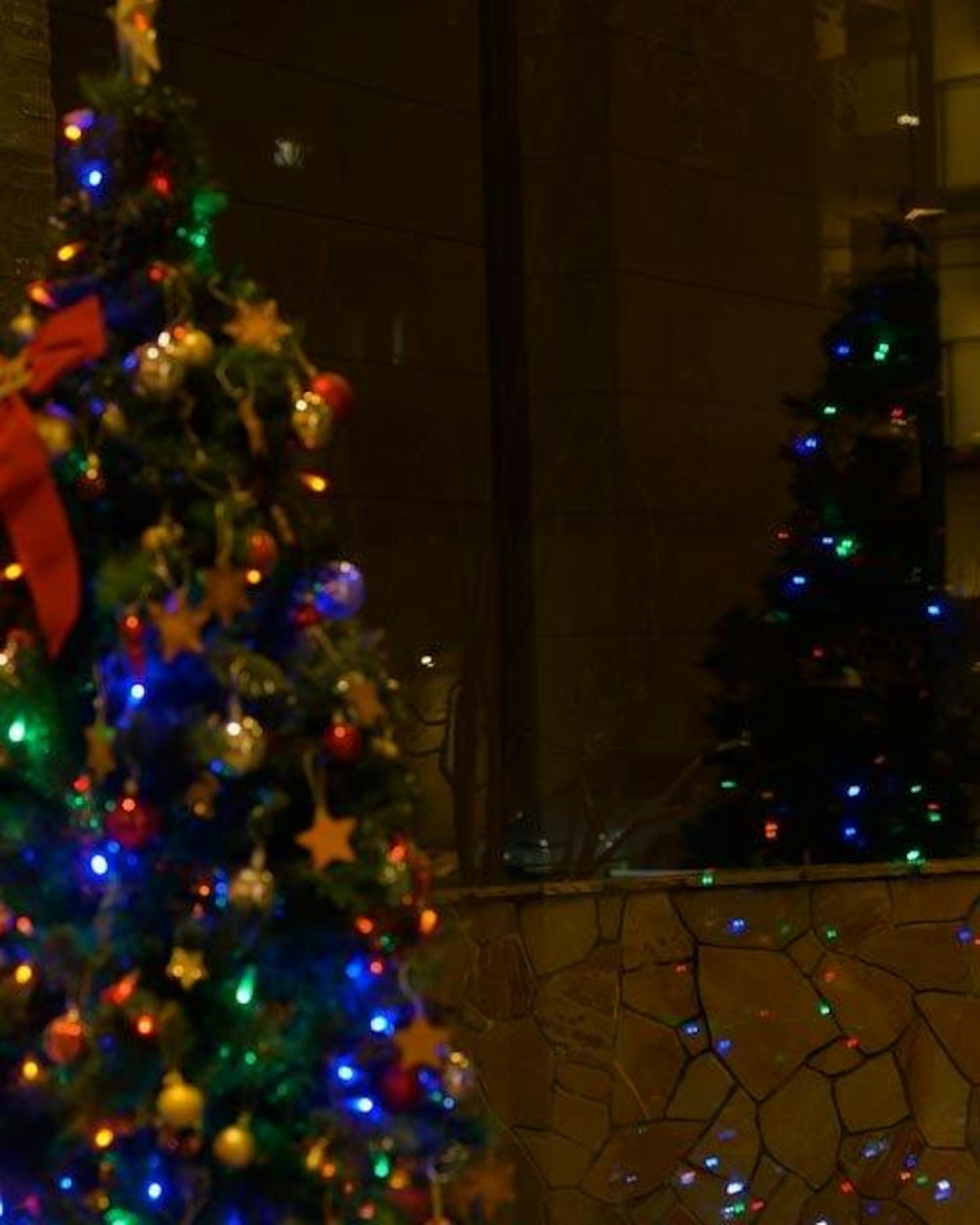 Christmas tree adorned with colorful lights and ornaments reflecting in a window
