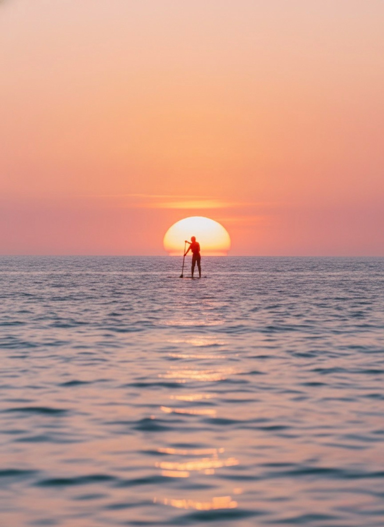 夕日を背景にしたスタンドアップパドルボードの人
