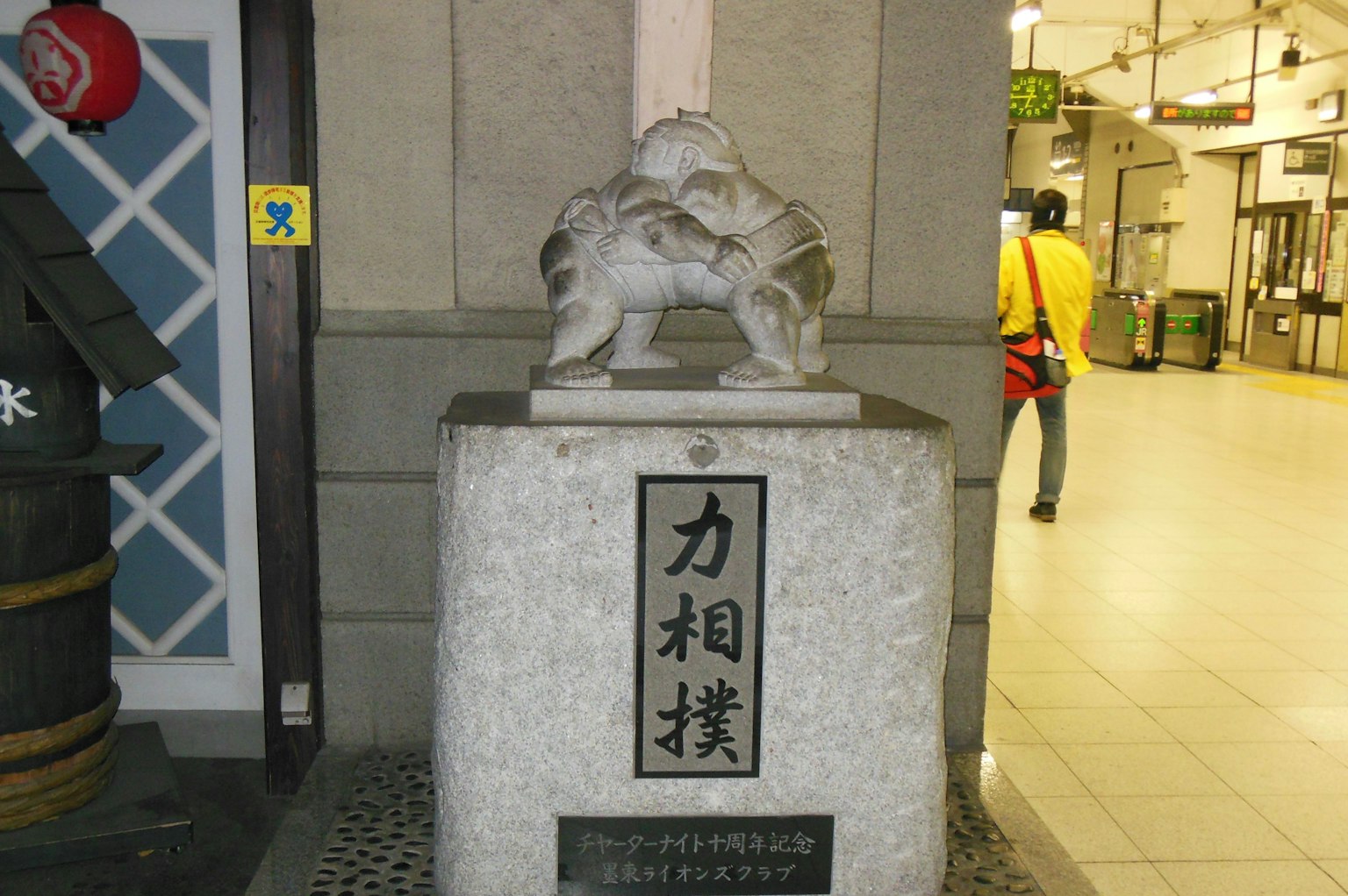 Sculpture d'un lutteur de sumo sur un piédestal en pierre près d'une gare