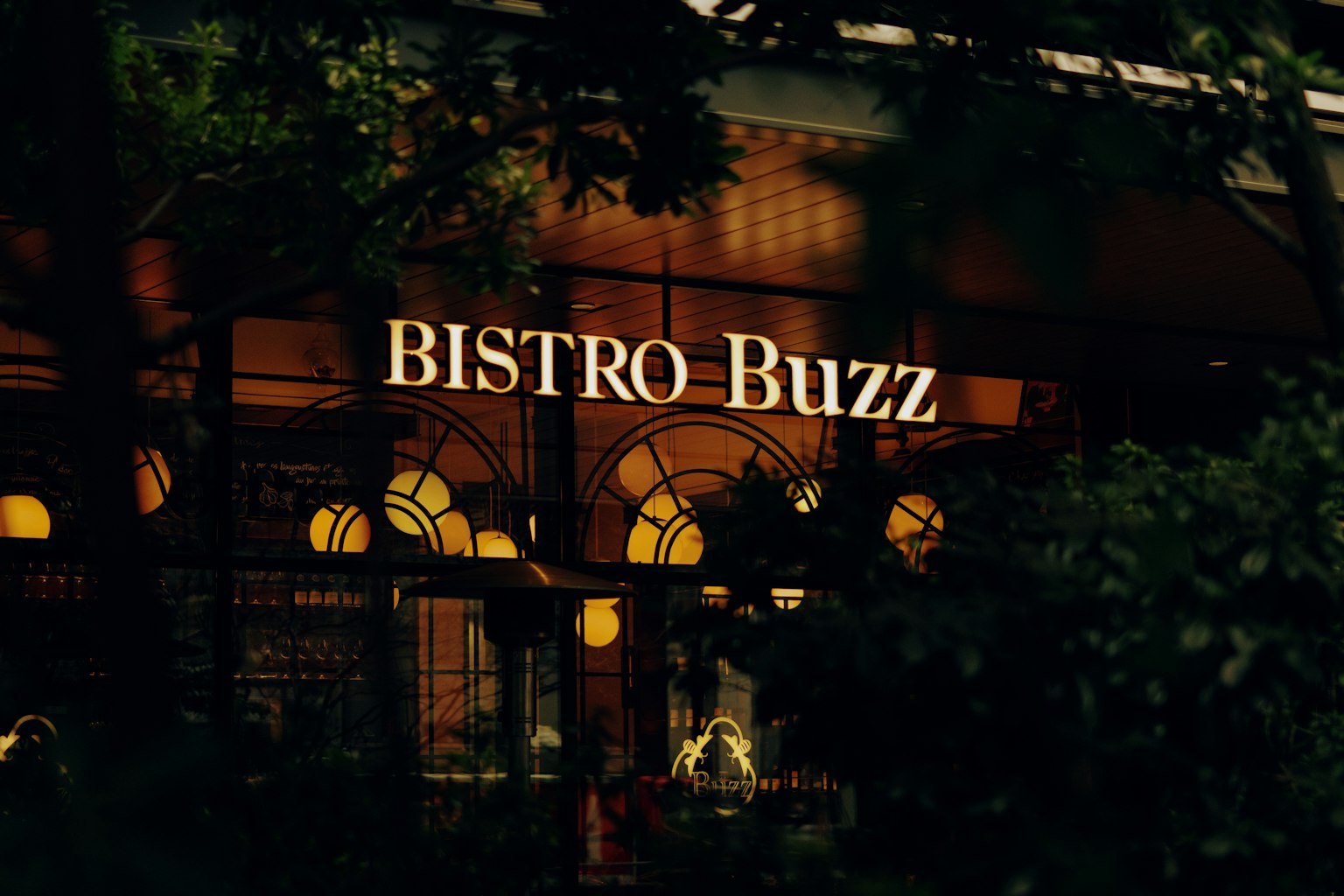 夜景中的Bistro Buzz招牌被植物环绕，温暖的灯光